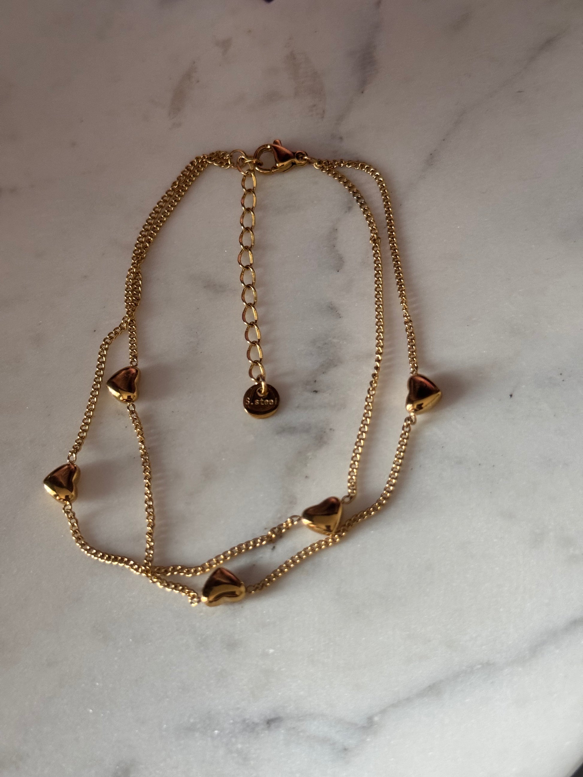 Gold bracelet with heart-shaped charms on a marble surface