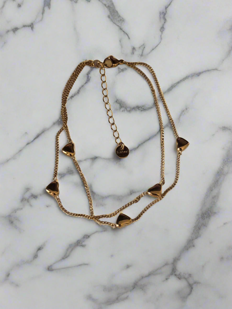 Gold chain bracelet with heart-shaped charms on a marble surface