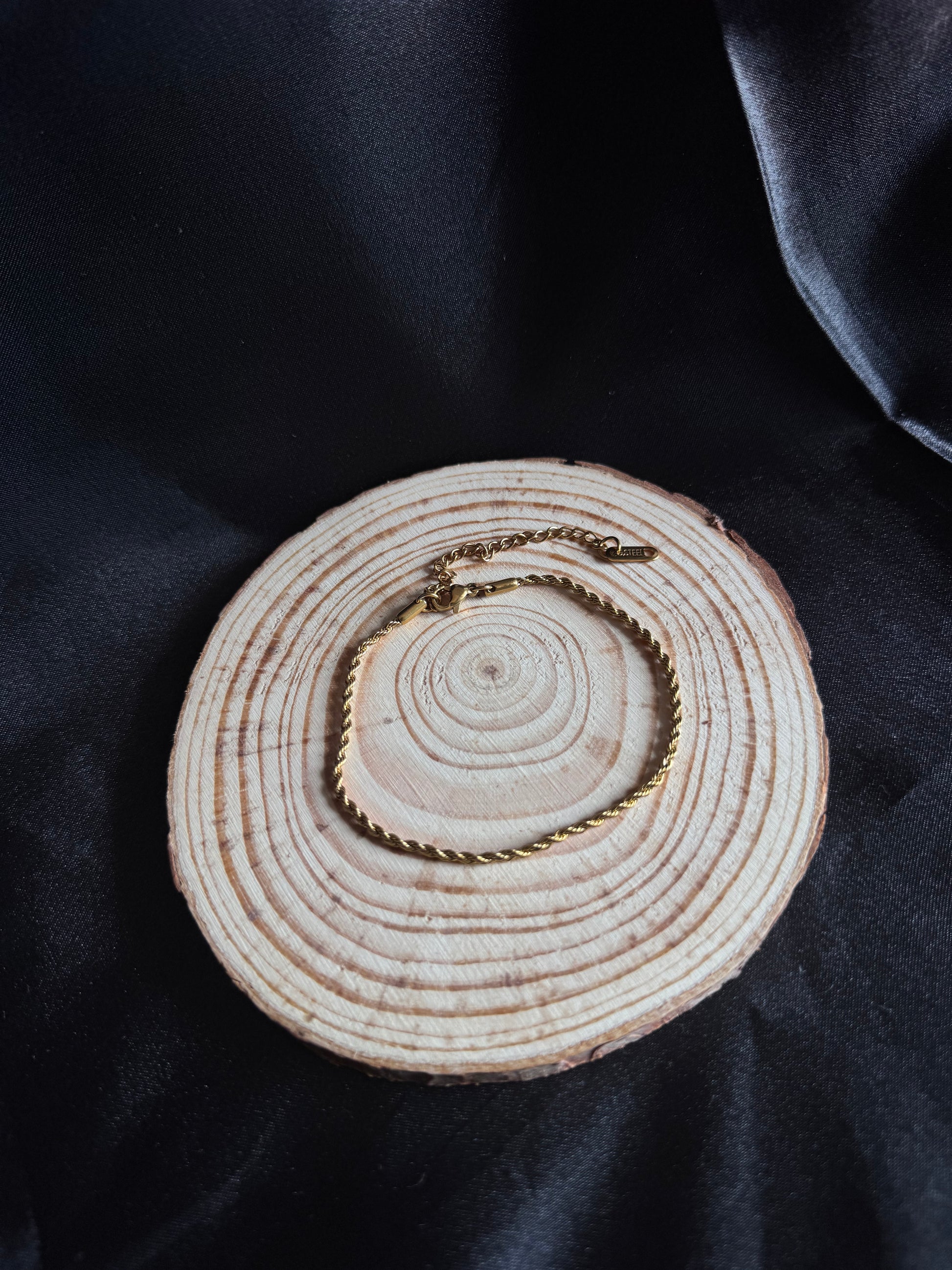 Gold rope anklet on a wooden circular object with a dark fabric background