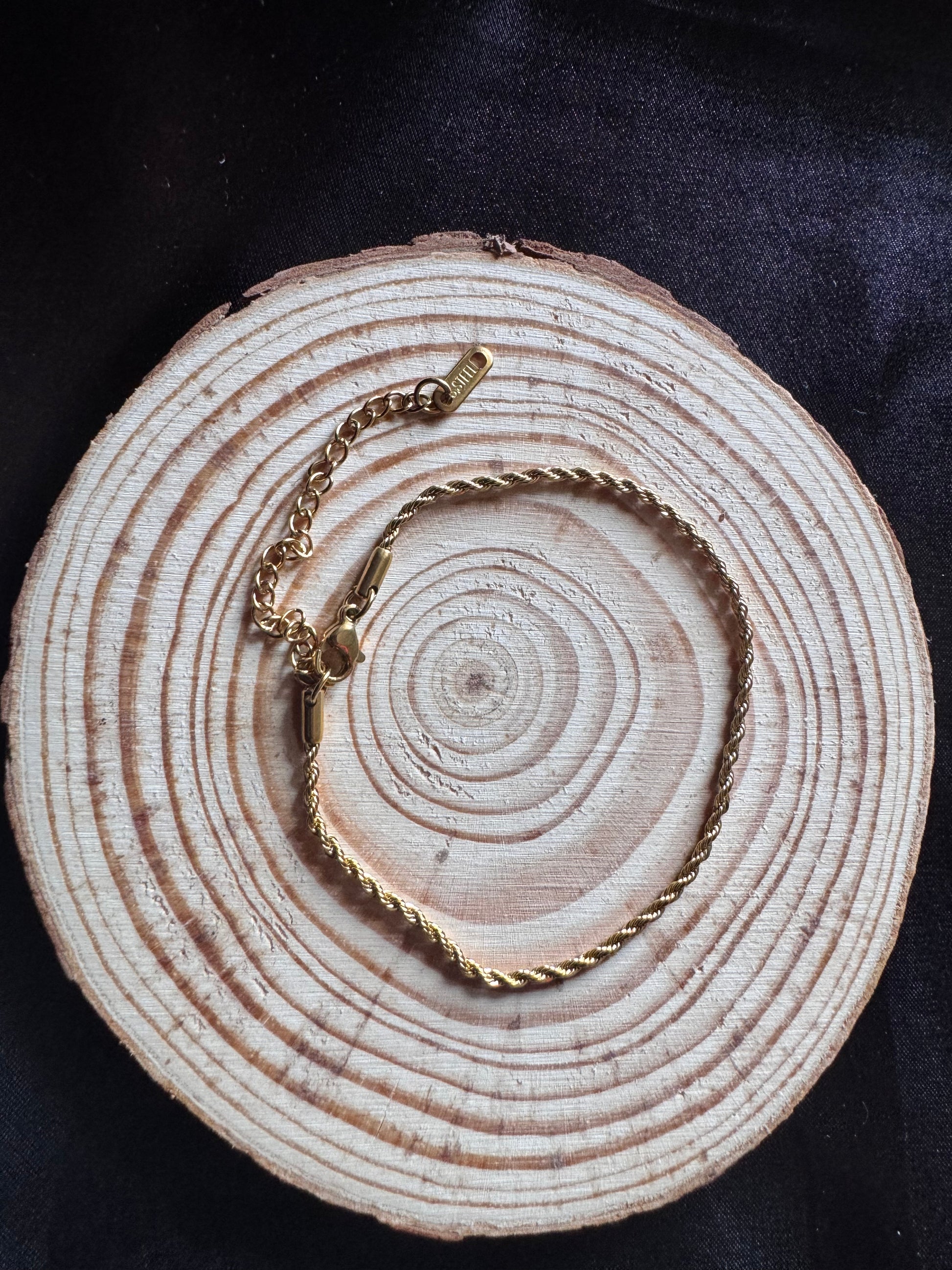 Gold rope anklet on a wooden surface with a dark background