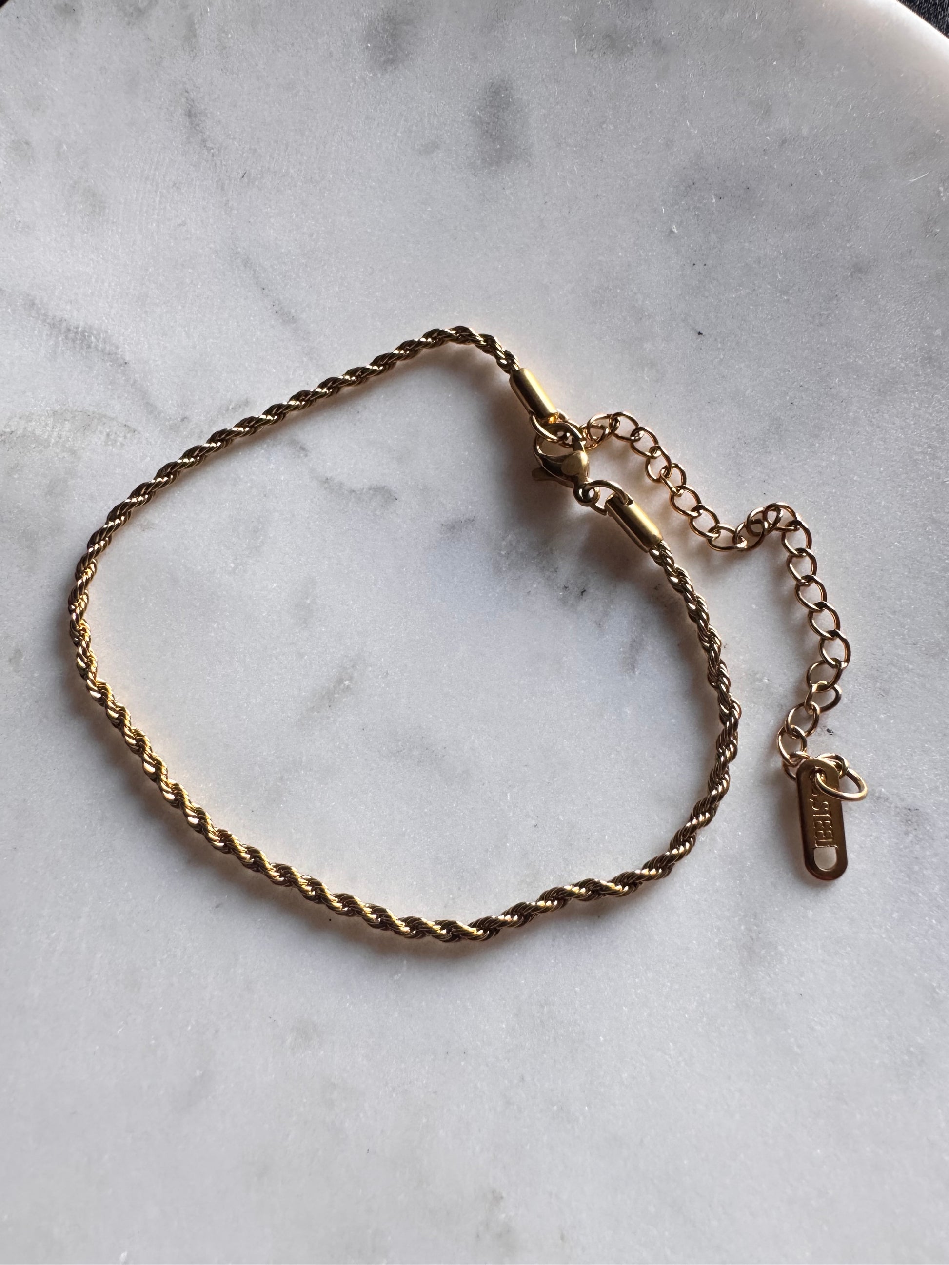 Gold rope anklet on a marble surface