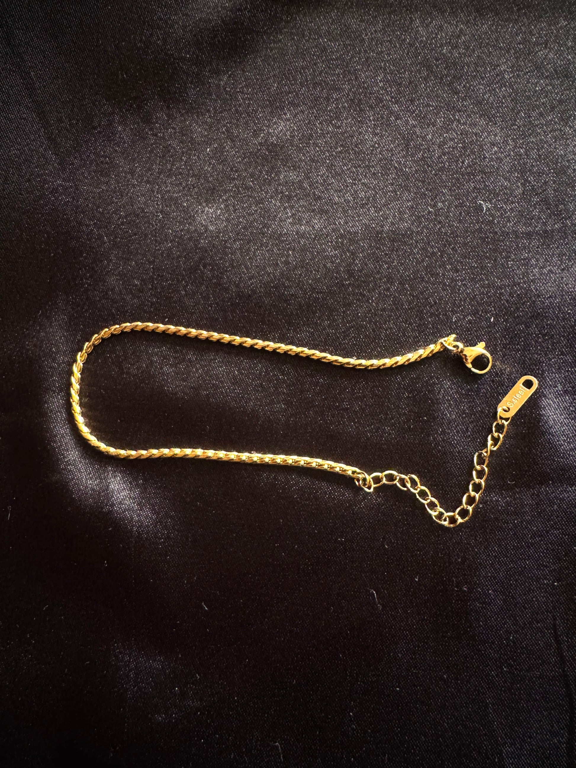 Gold twist rope anklet on a black fabric background