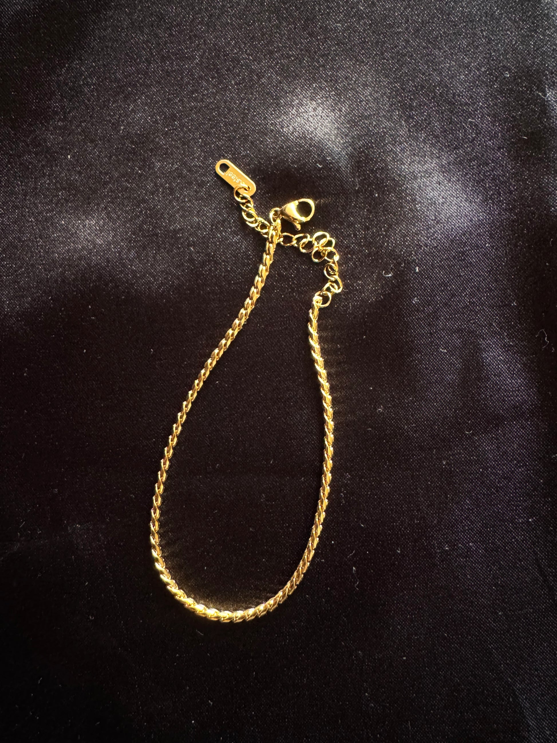 Gold twist rope anklet on a black textured background