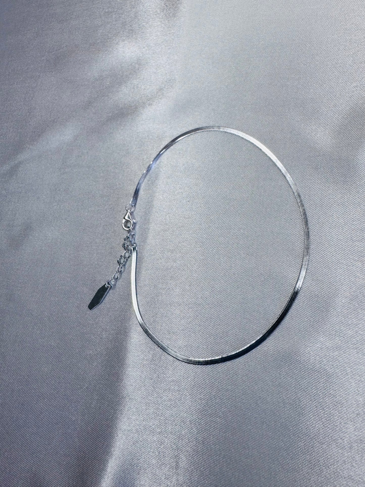 Silver anklet on a gray fabric background