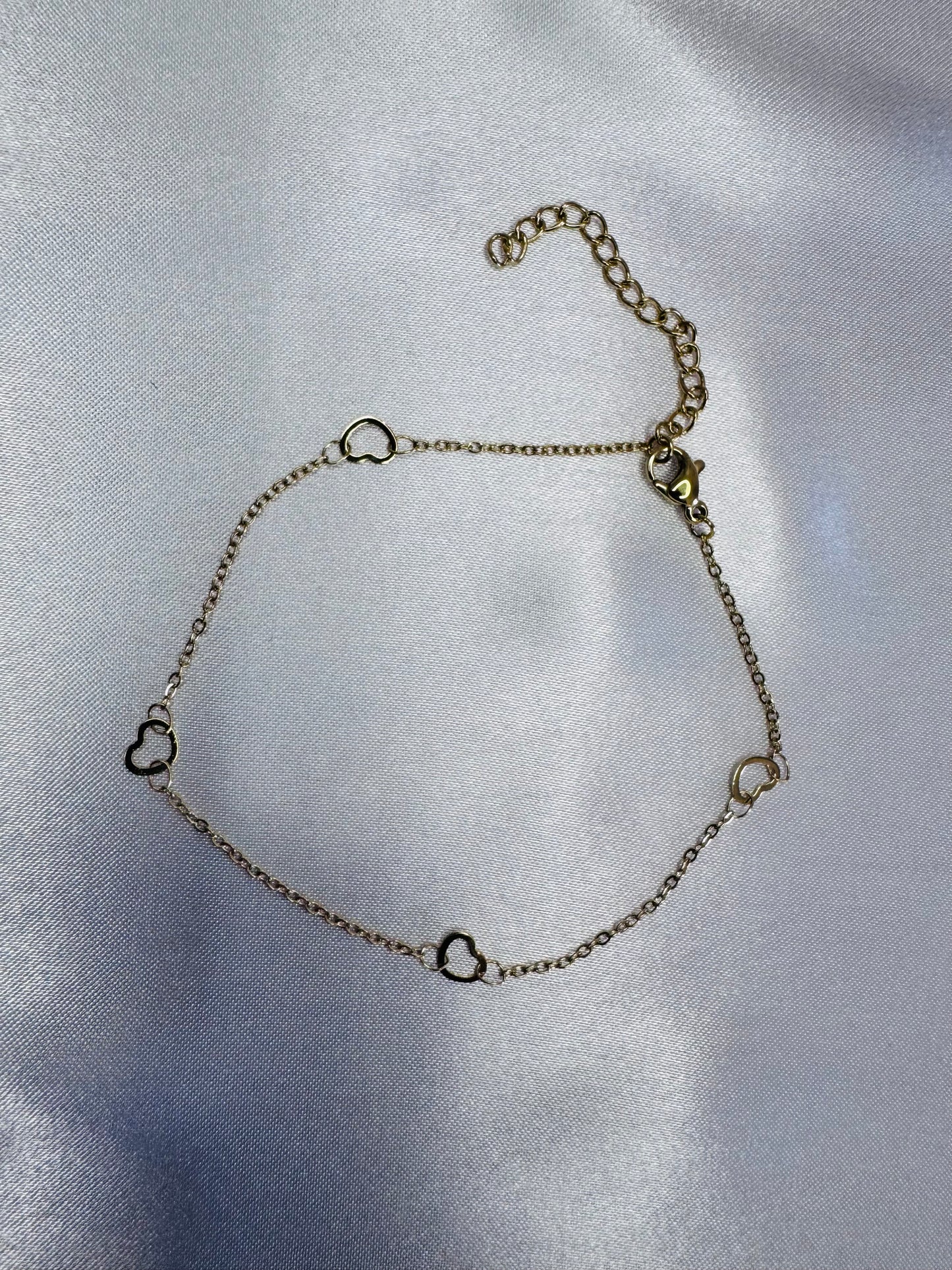 Silver chain anklet with heart-shaped links on a light gray background