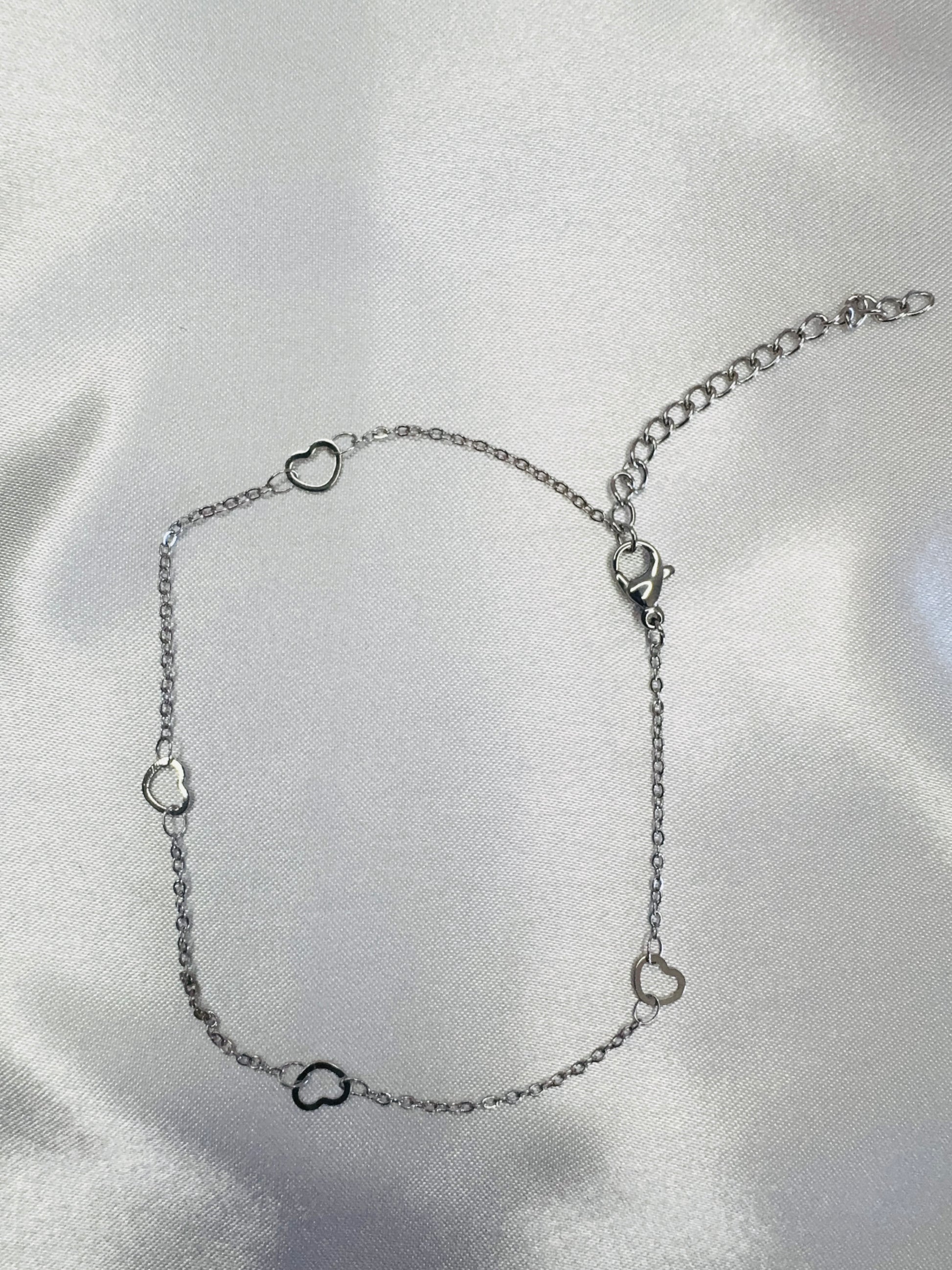 Silver anklet with heart-shaped charms on a light gray background