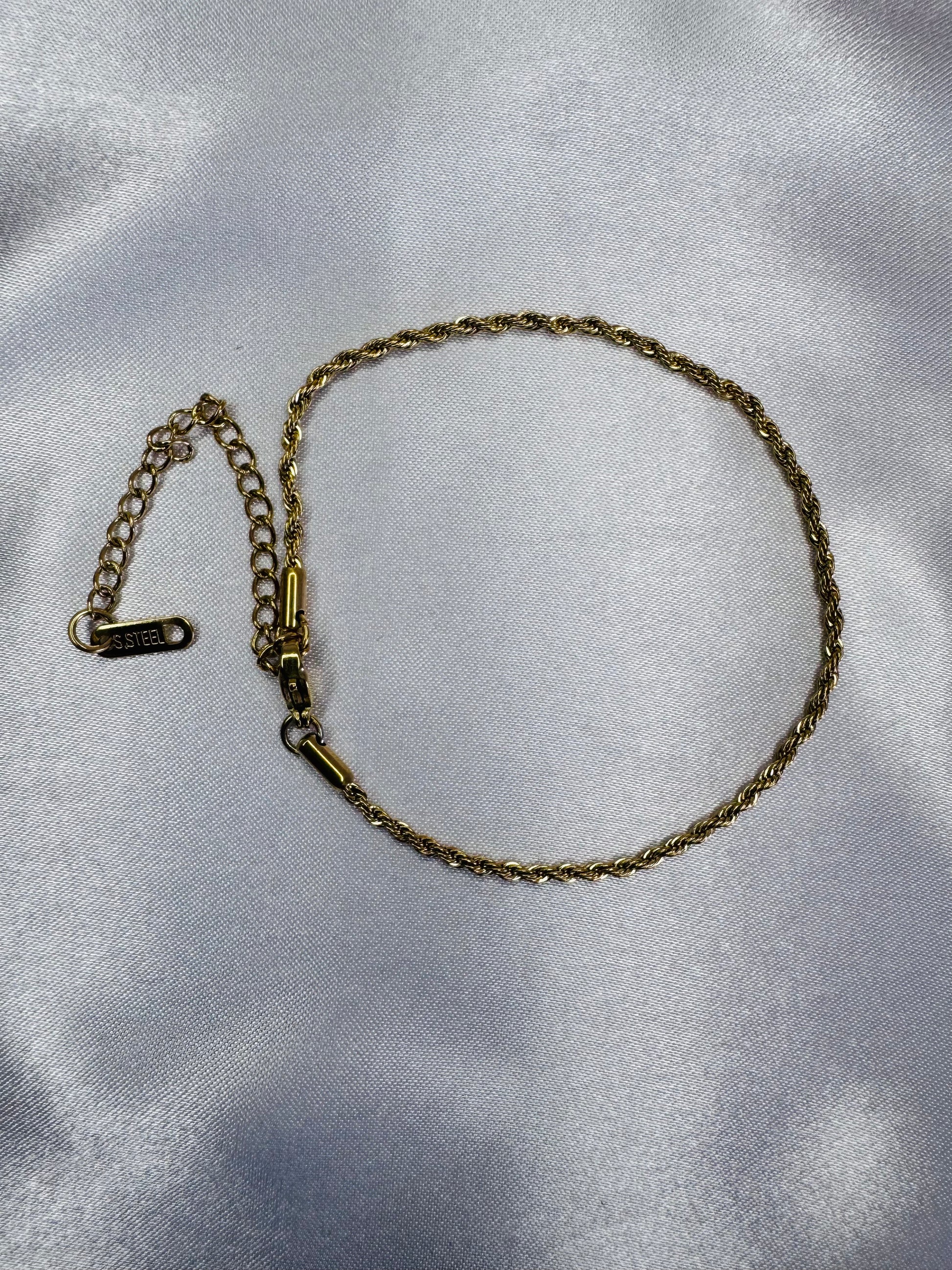 Gold rope anklet on a silver satin background