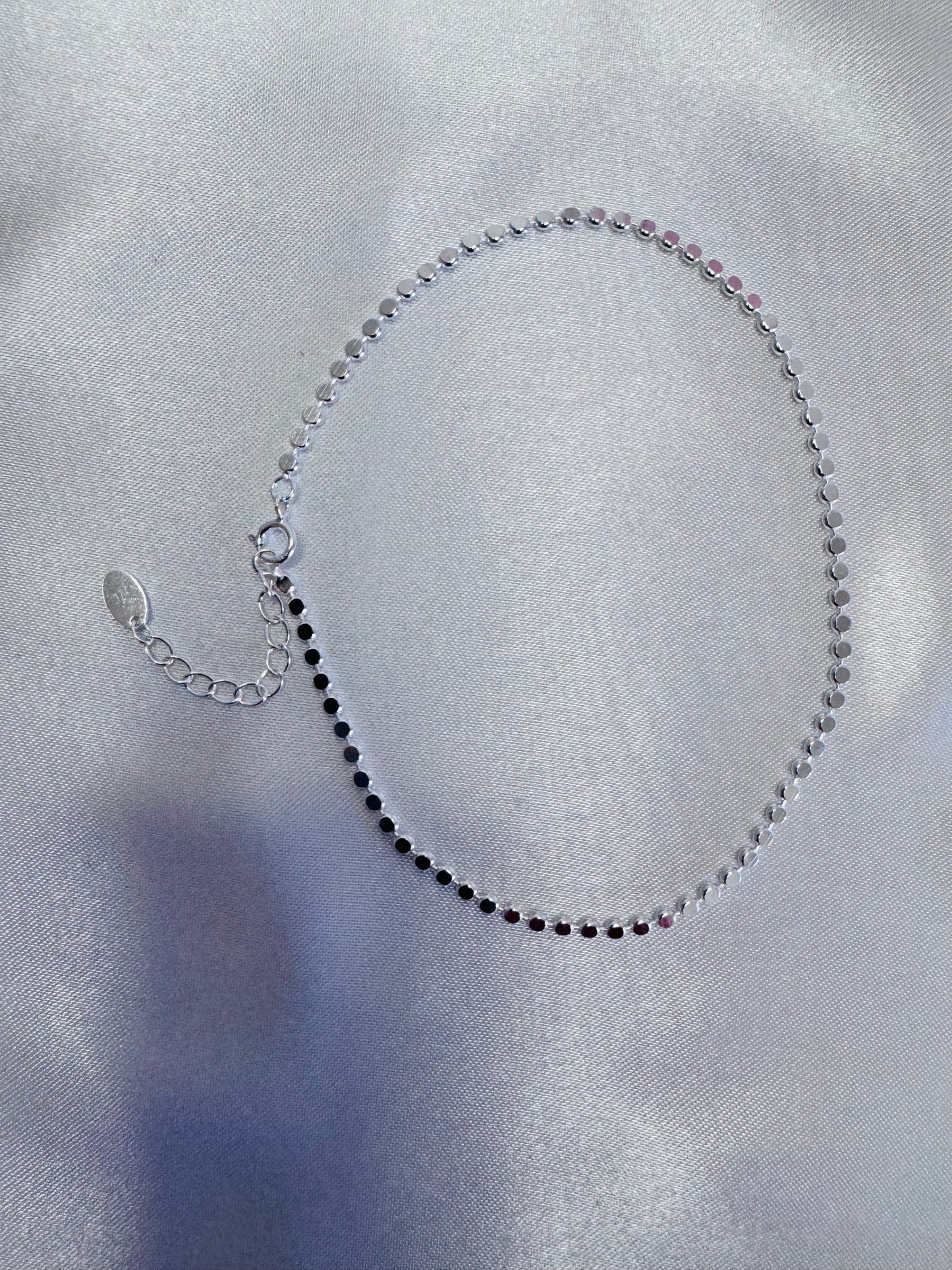 Silver shimmer anklet on a light gray fabric background
