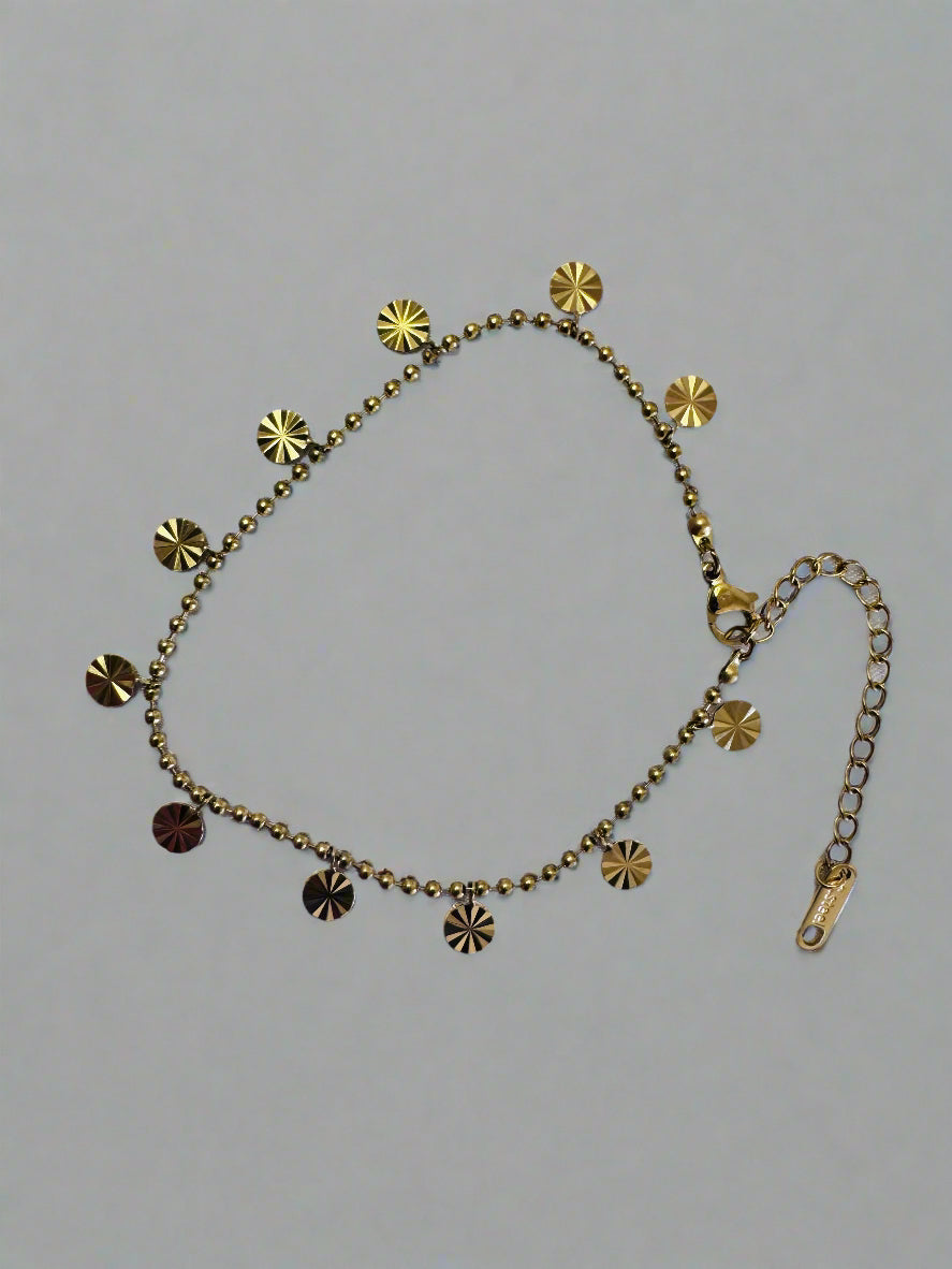 Gold anklet with disc-shaped charms on a gray background