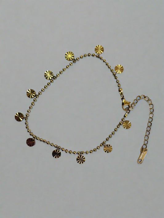 Gold anklet with disc-shaped charms on a gray background