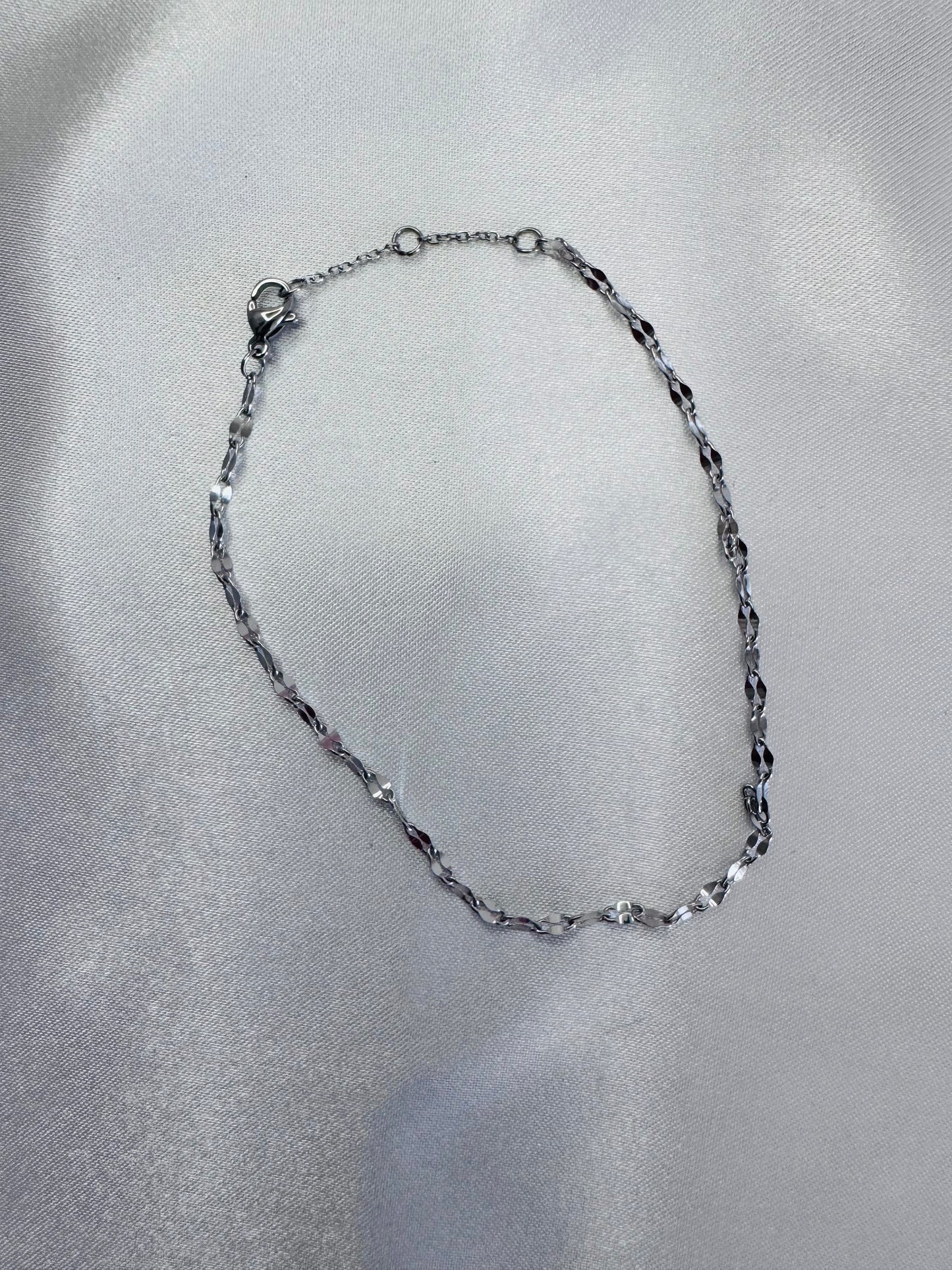 Silver twinkle anklet on a gray fabric background