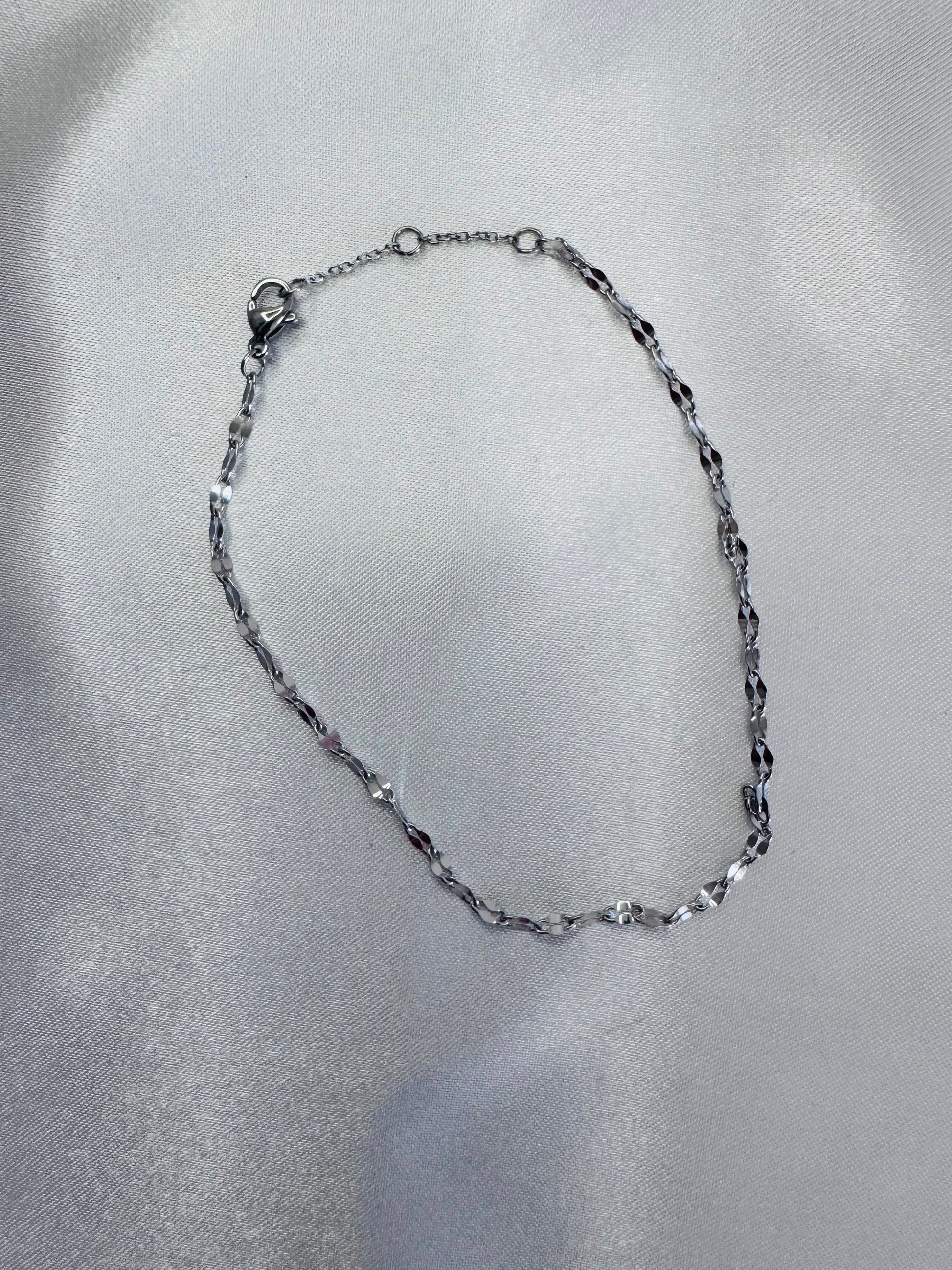 Silver twinkle anklet on a gray fabric background