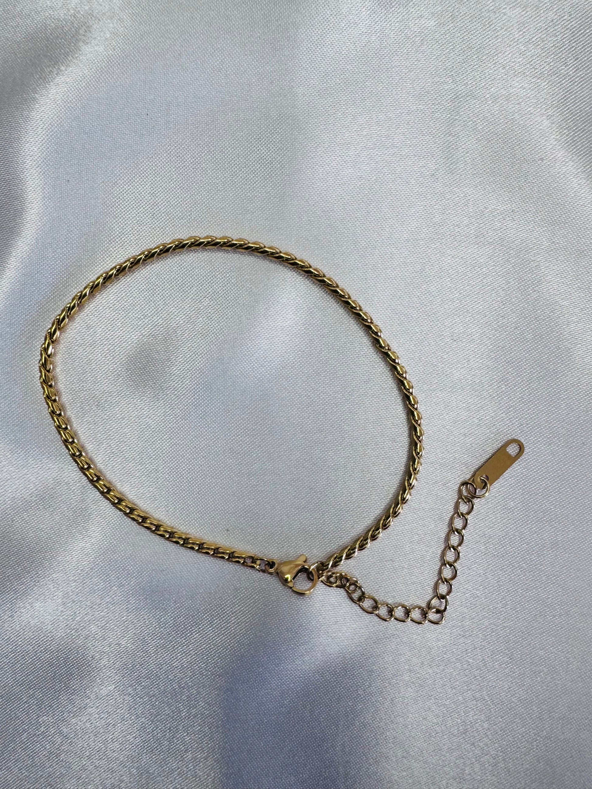 Gold twist rope anklet on a light gray fabric background