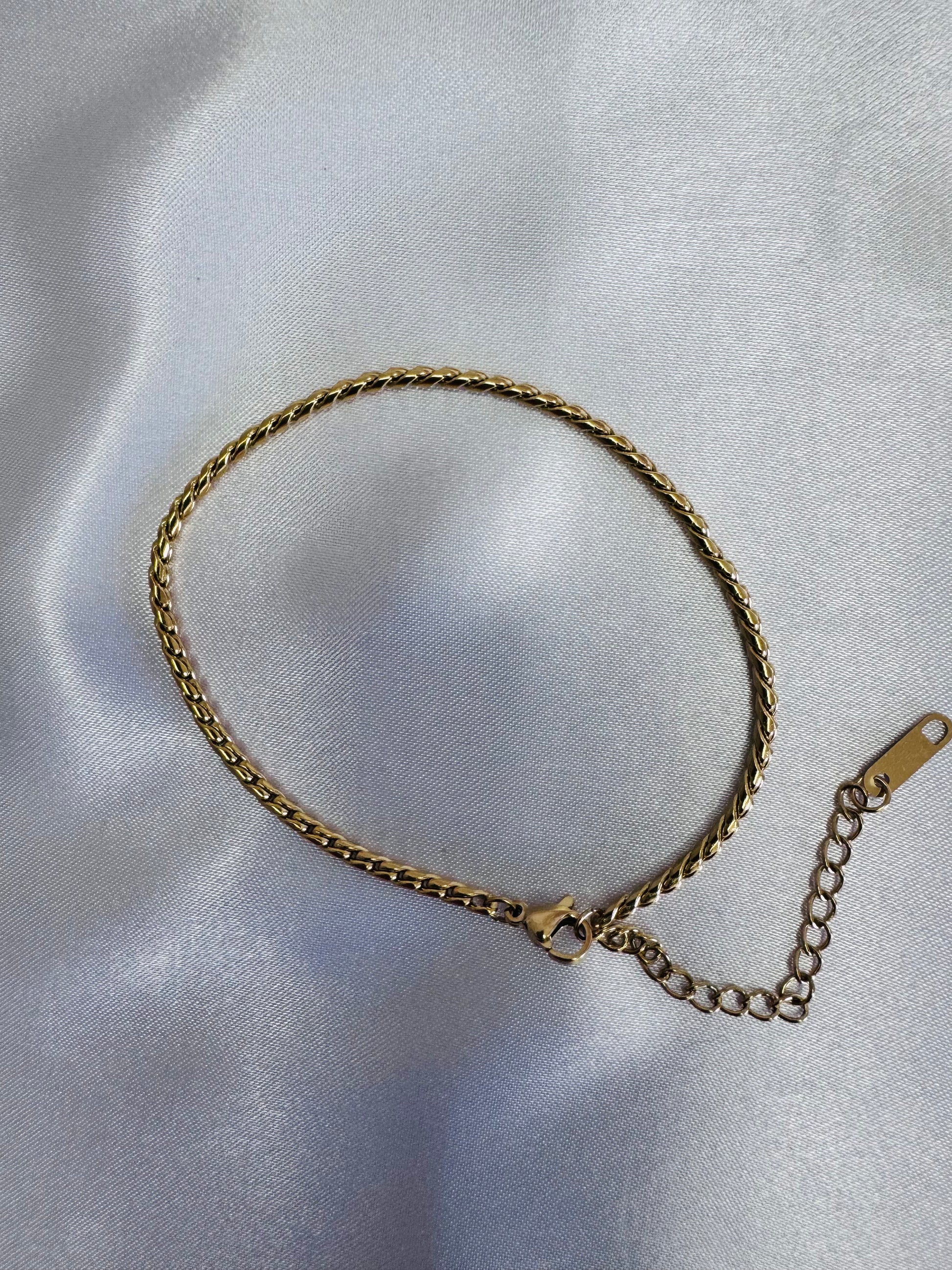 Gold twist rope anklet on a light gray fabric background