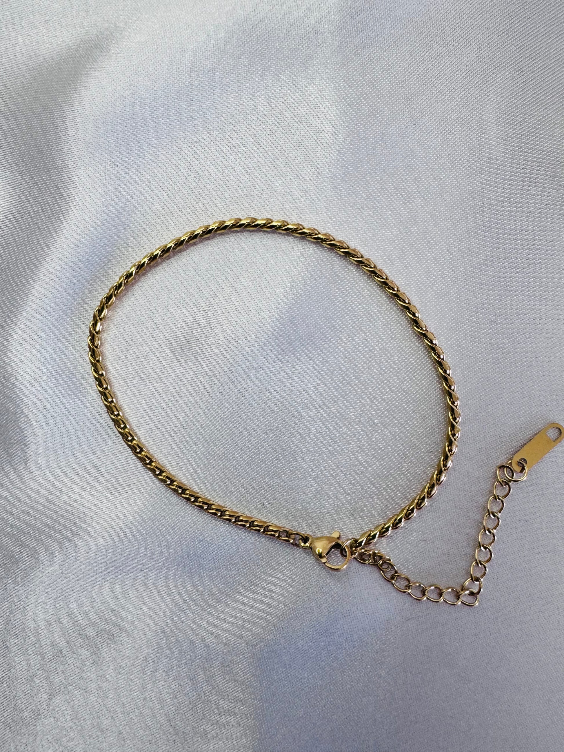 Gold twist rope anklet on a light gray fabric background