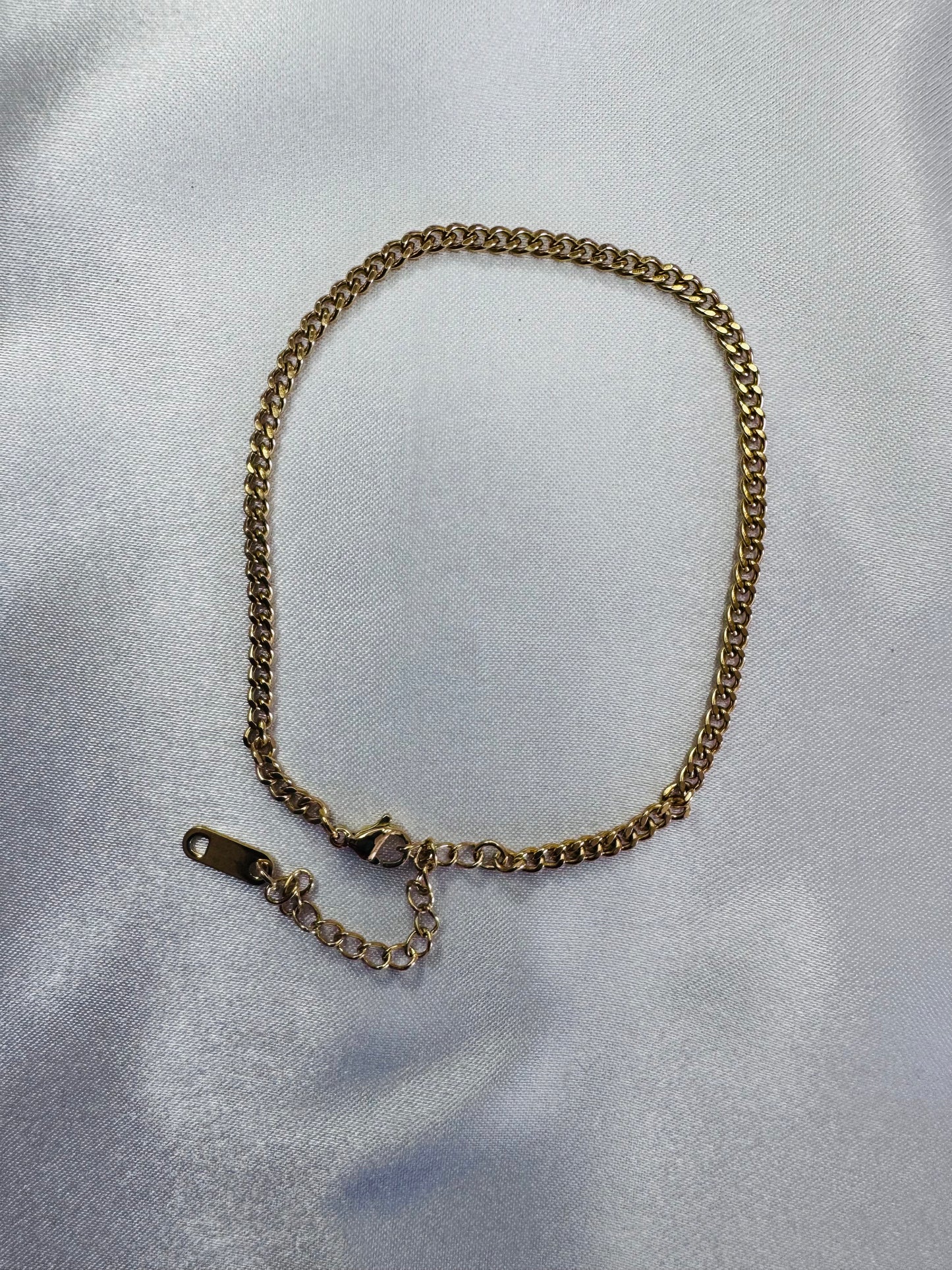 Gold chain anklet on a light gray fabric background