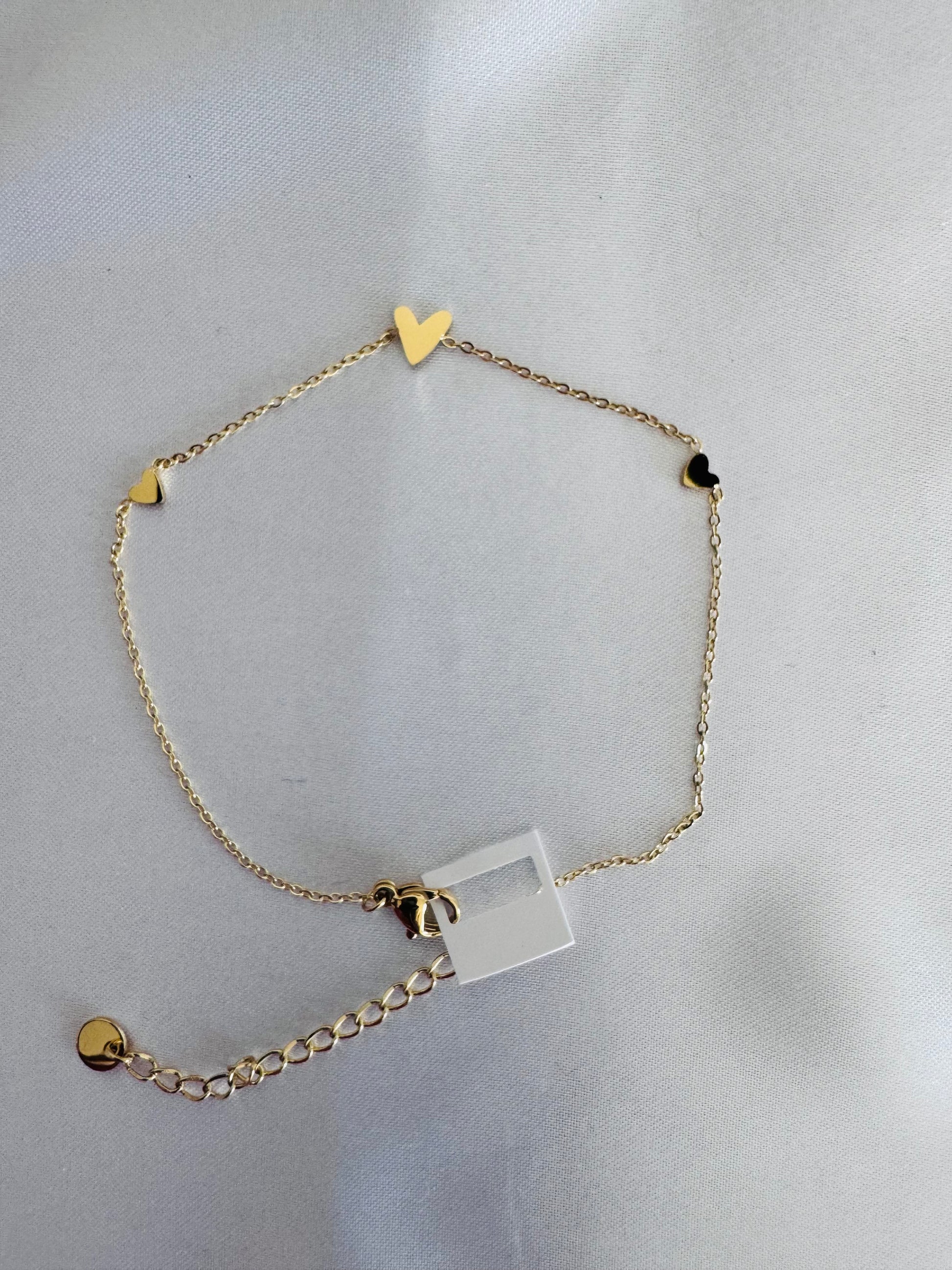 Gold anklet with heart and square charm on a light gray background