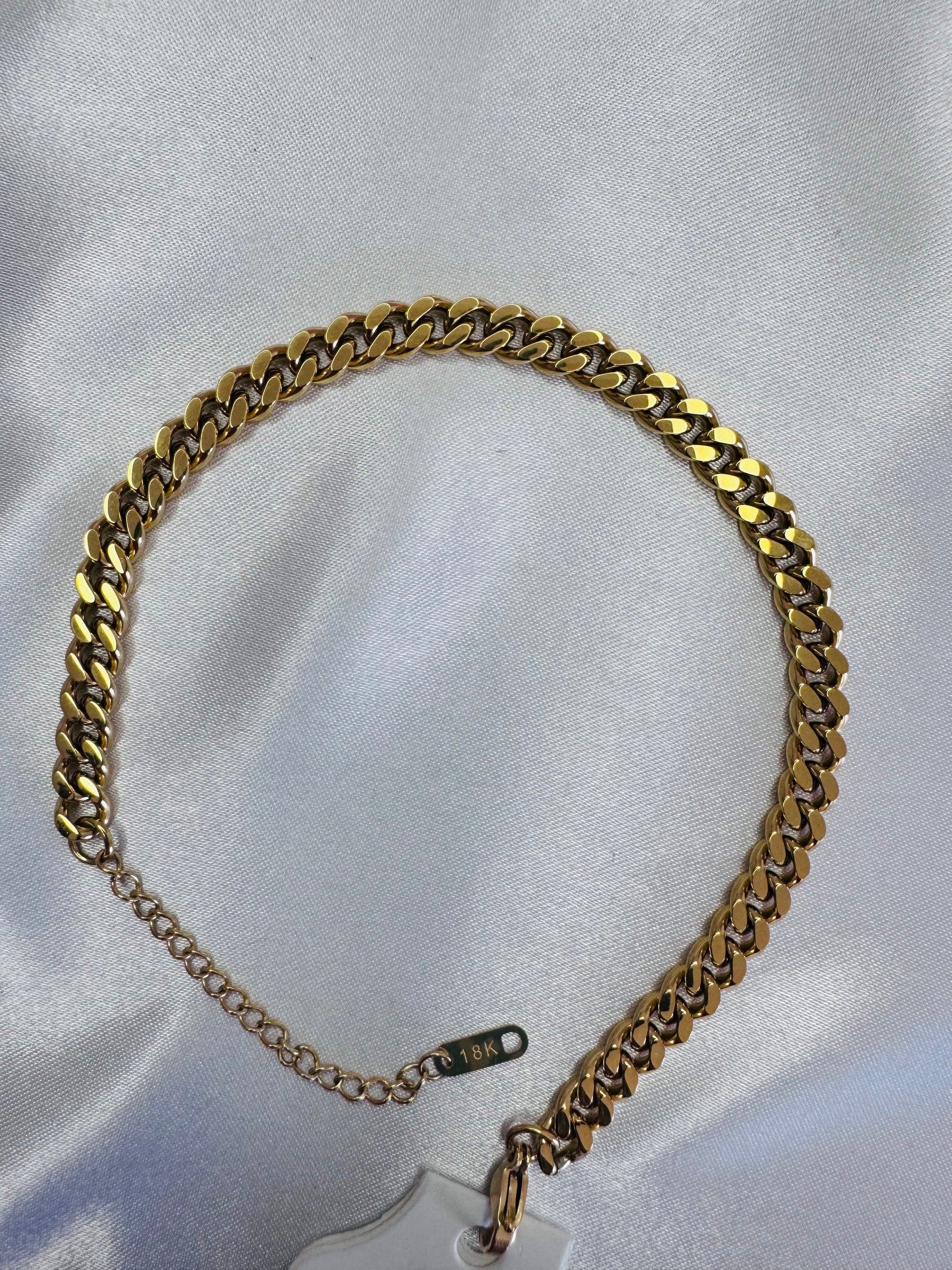 18k cuban link anklet on a white fabric background
