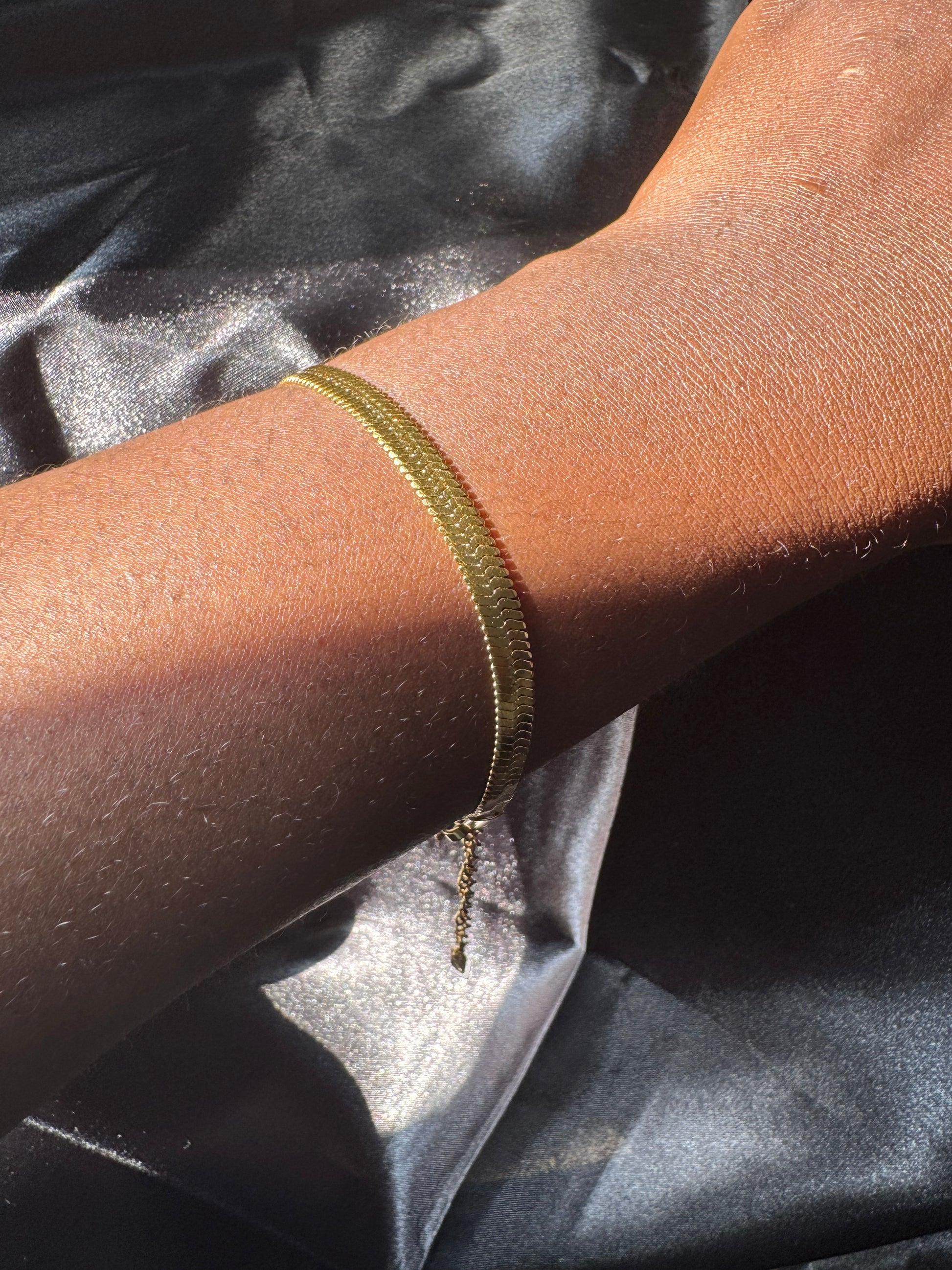 Gold bracelet on a wrist with a dark fabric background