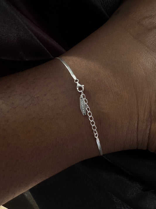 Silver anklet on an ankle with a dark background