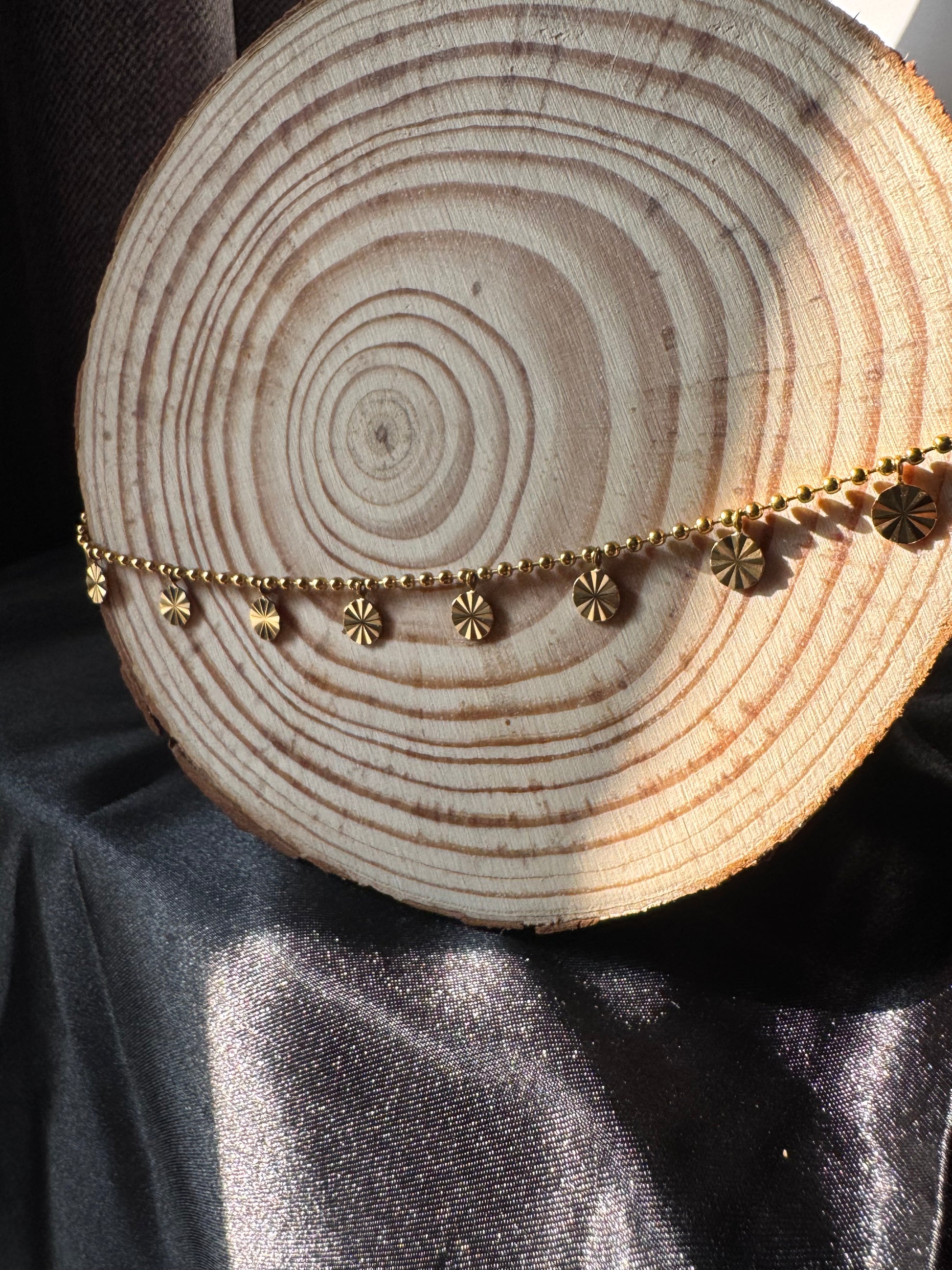 Gold chain anklet on a wooden log with a dark fabric background