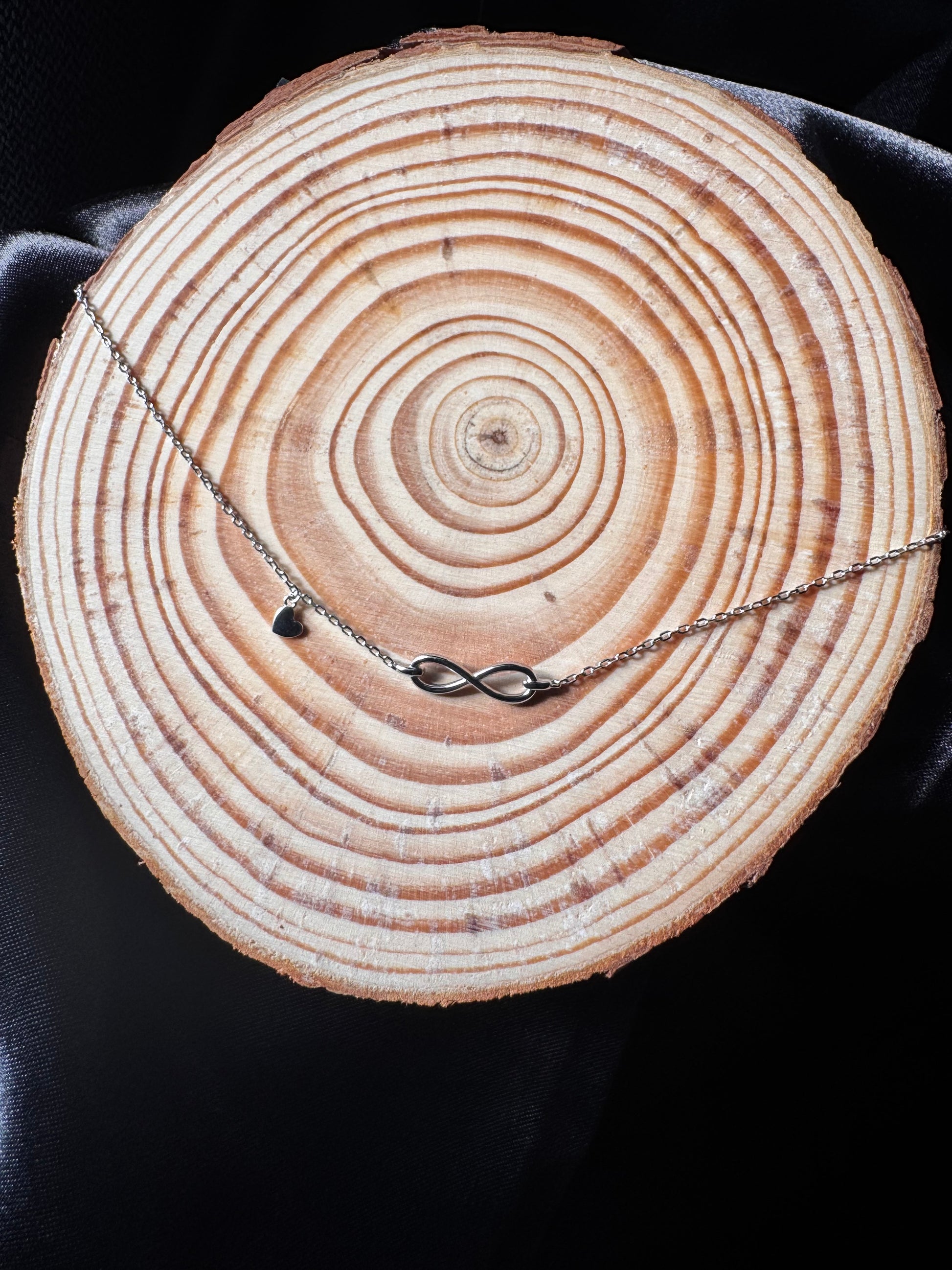 Anklet with an infinity symbol draped over a wooden log with annual rings.