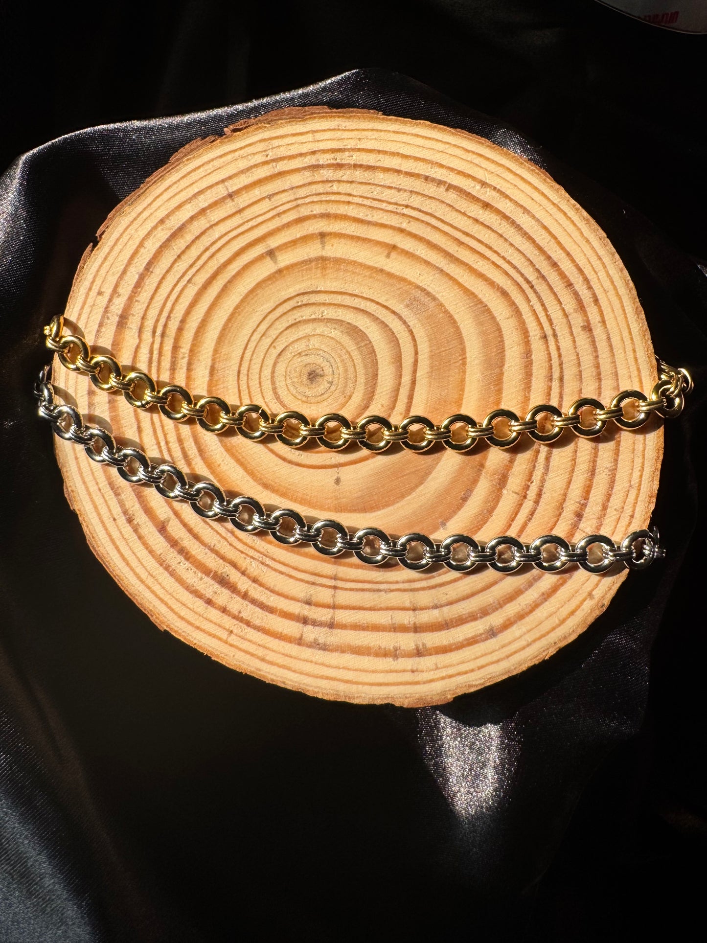Two chains, one gold and one silver, draped over a wooden surface with a black background.