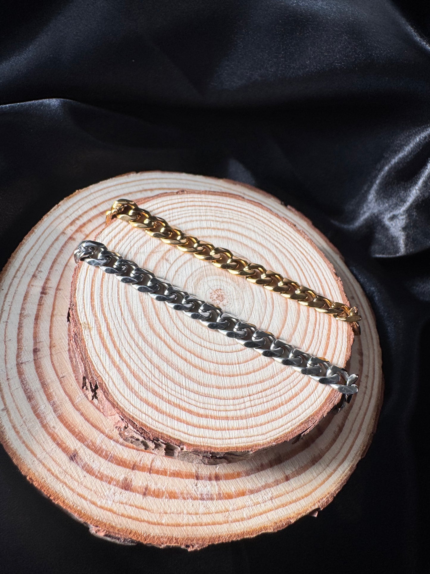 Two gold and silver chain anklets on a wooden surface with black fabric background