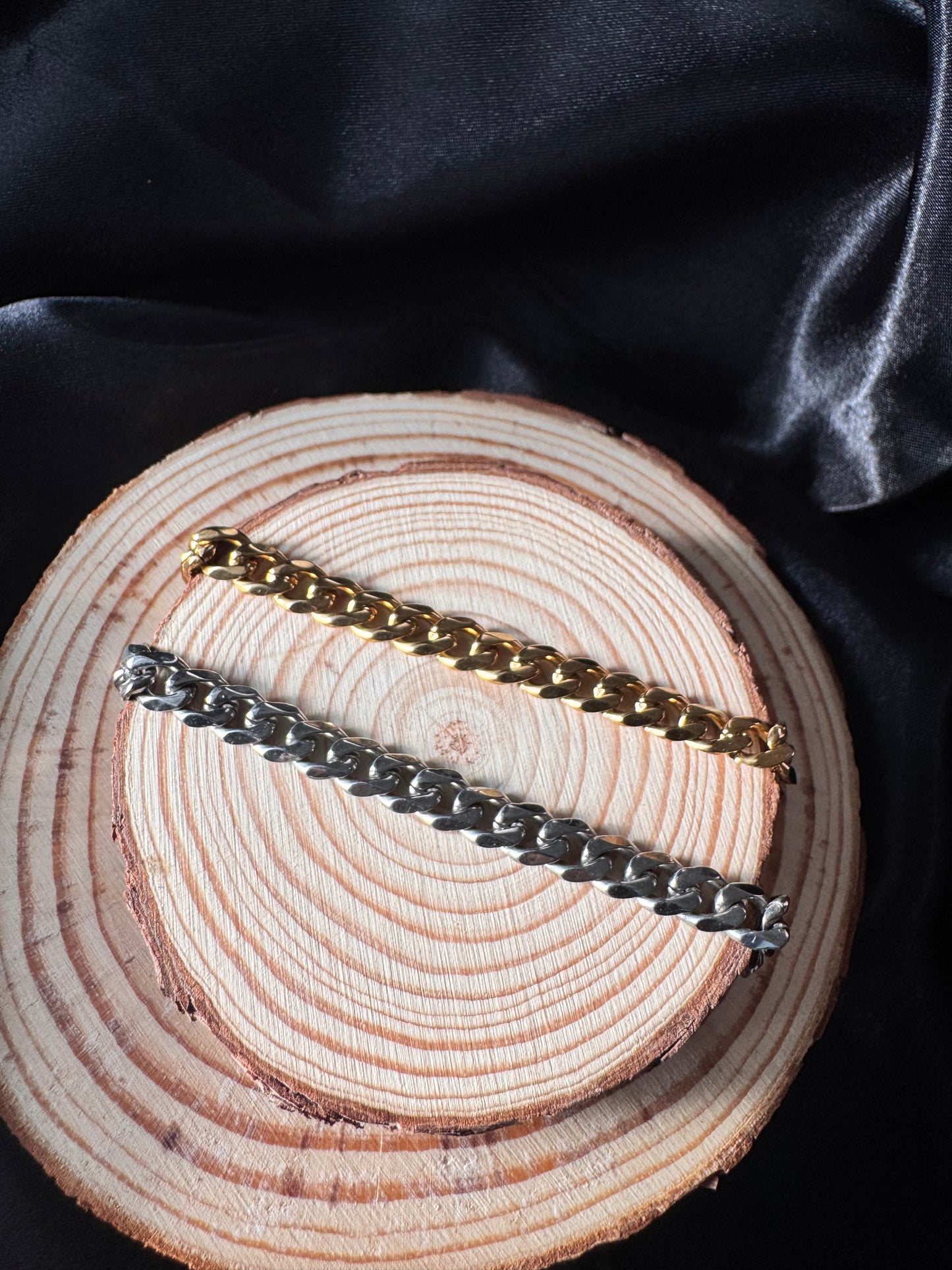 Two gold and silver chain anklets on a wooden surface with black fabric background