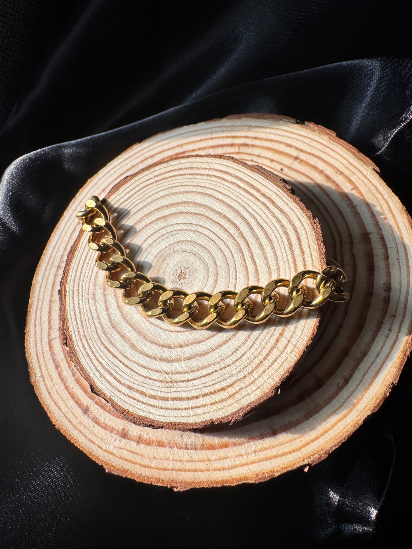 Gold chain  anklet on a wooden surface with a dark fabric background