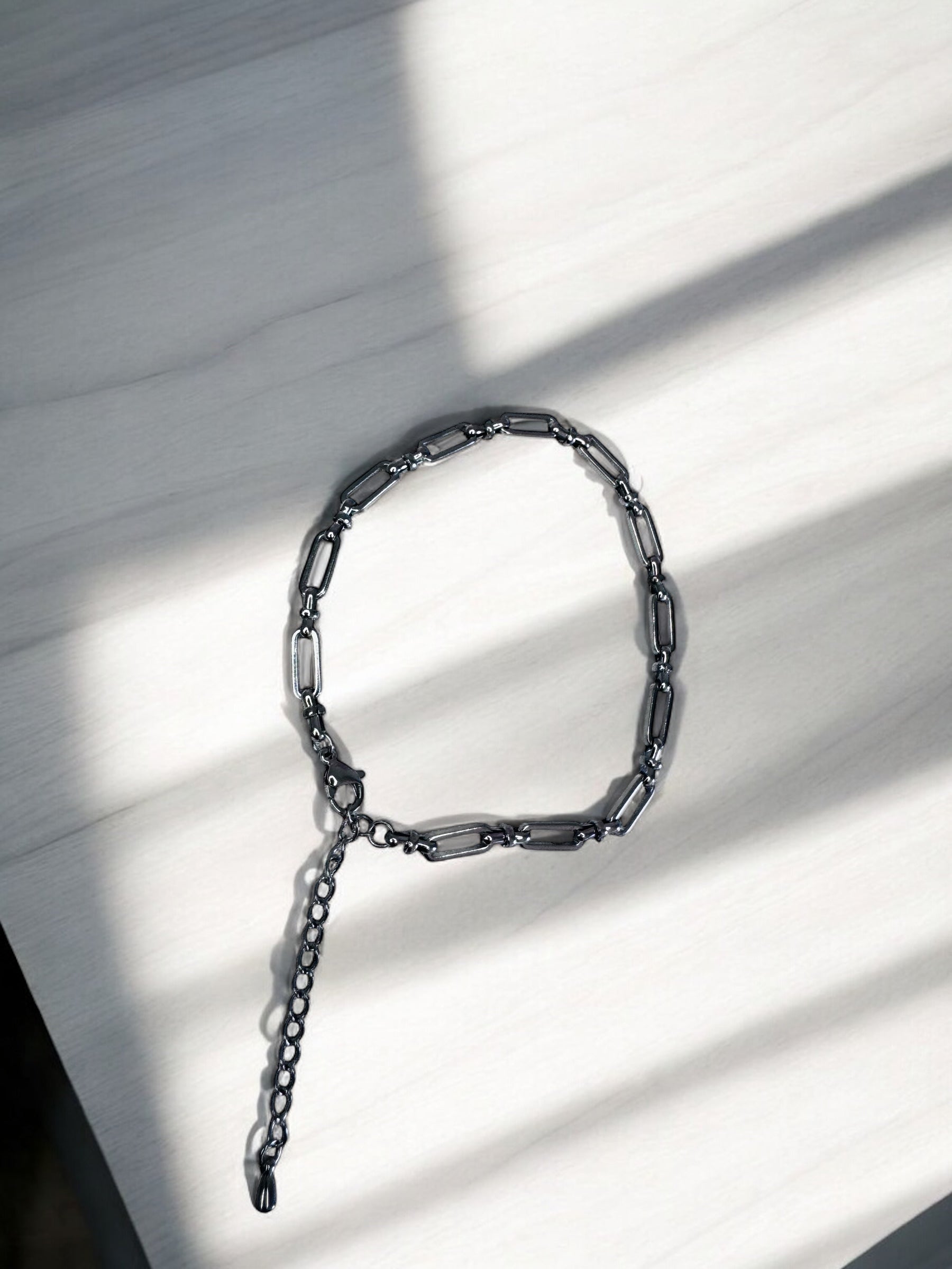 Silver bold link anklet on a light wooden surface with shadows