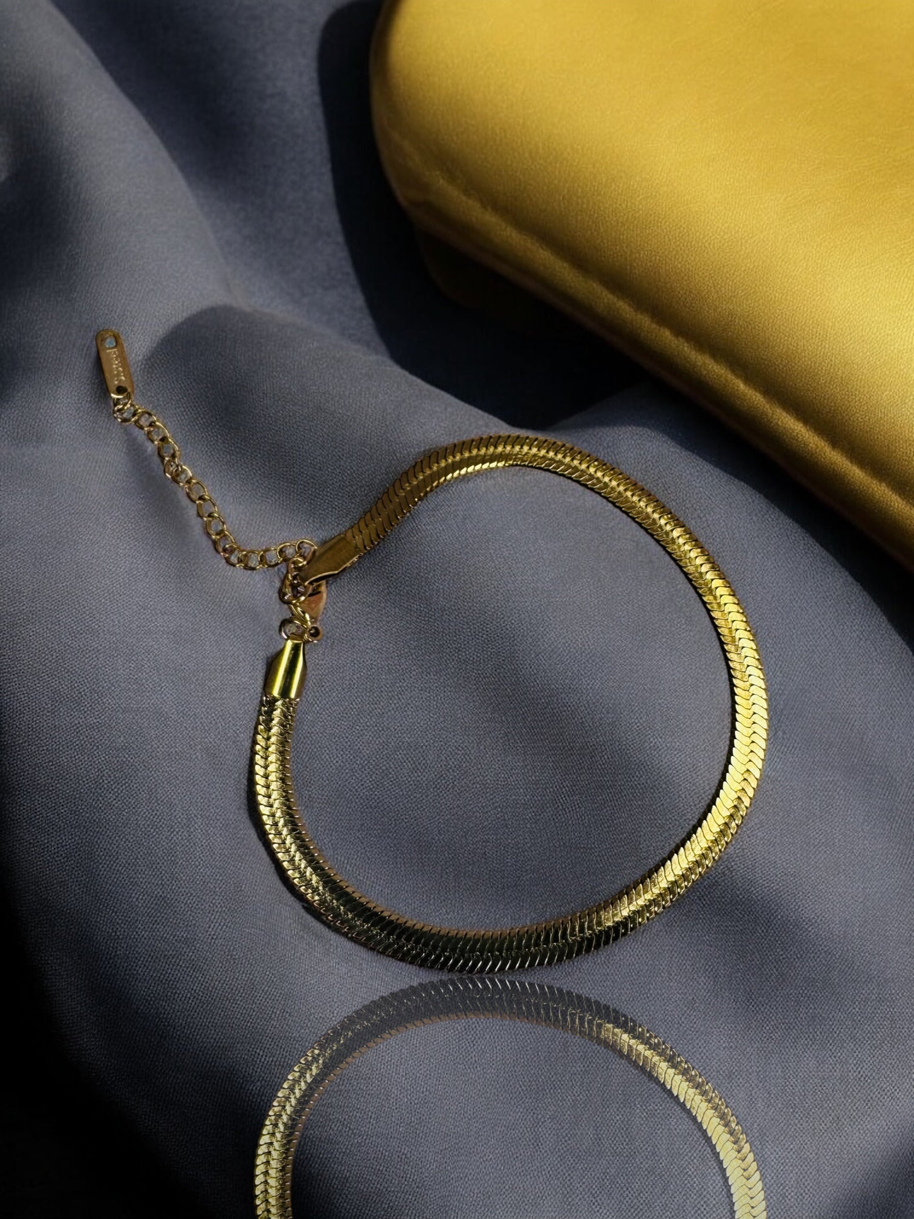 Gold snake chain necklace on a reflective surface with a gold box in the background