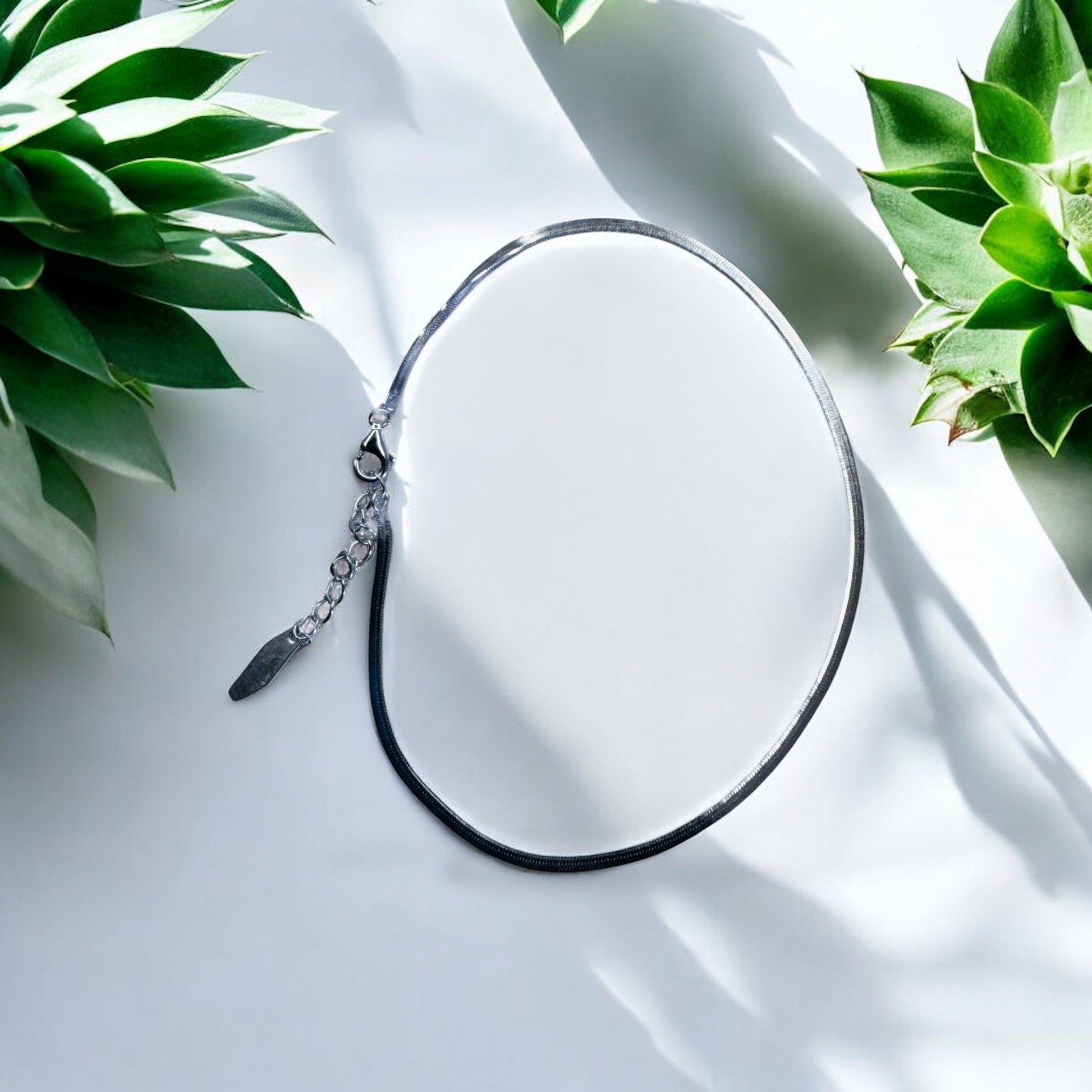 silver anklet on a white surface with green plants