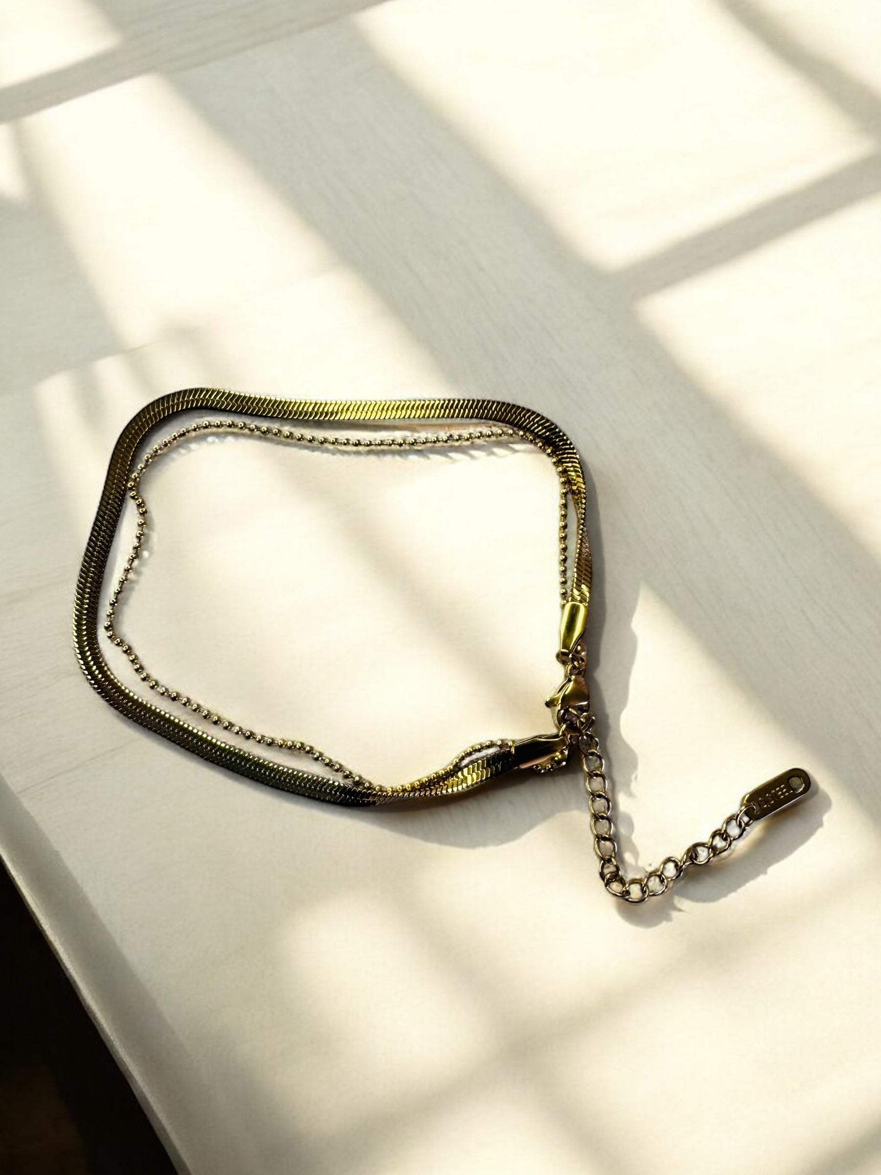 Gold chain necklace on a light surface with shadows