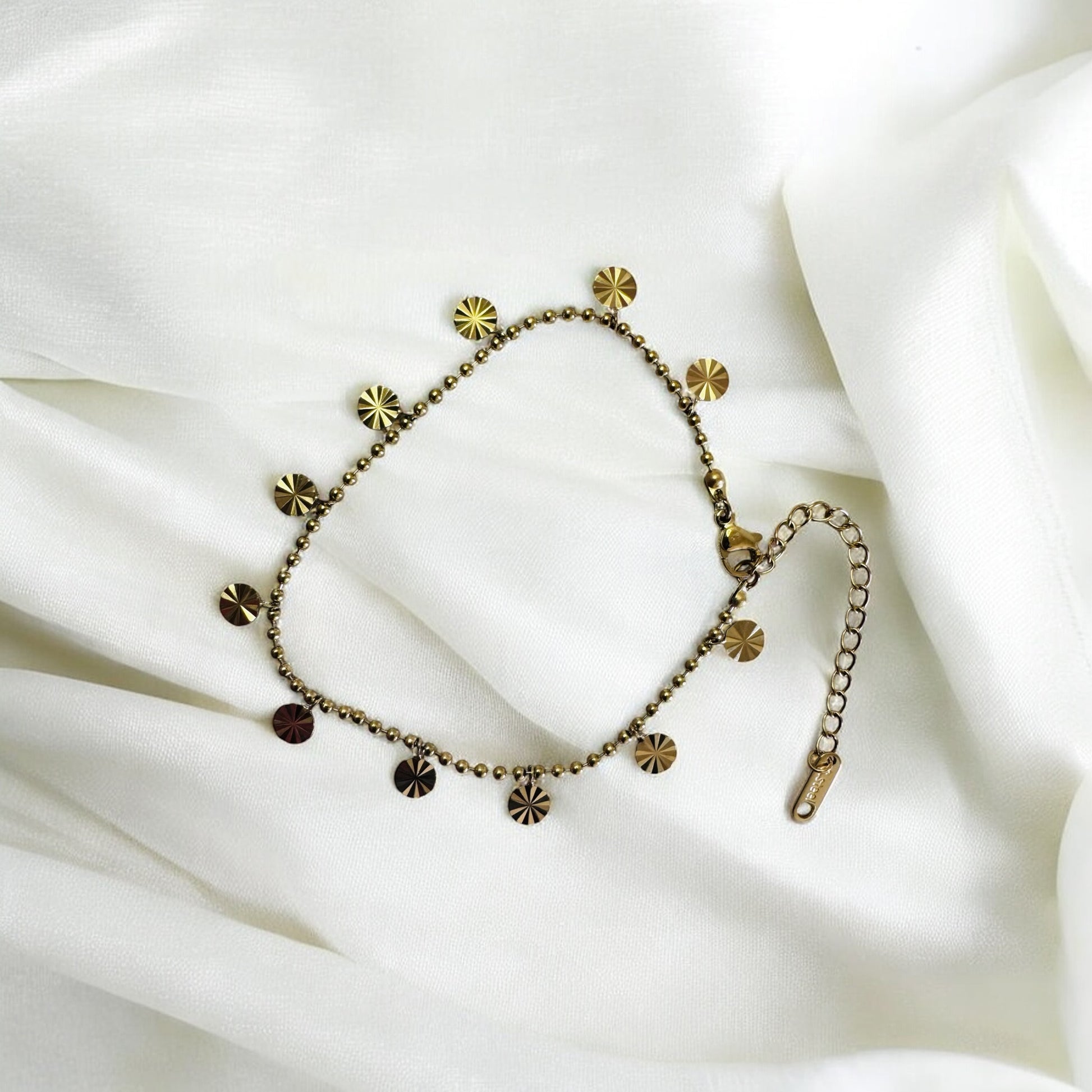 Gold anklet with disc designs on a white fabric background