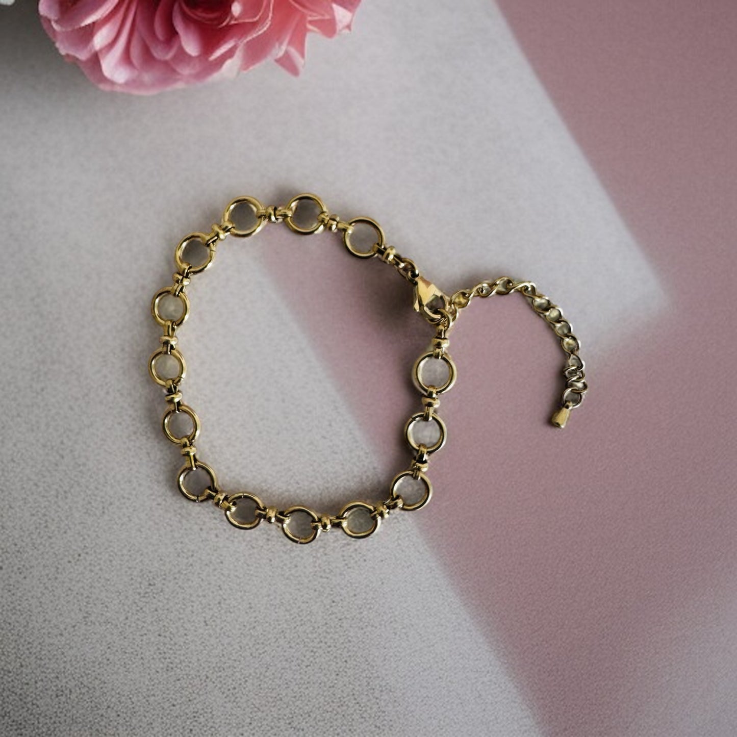 Gold chain anklet  on a light pink surface with a pink flower in the corner.