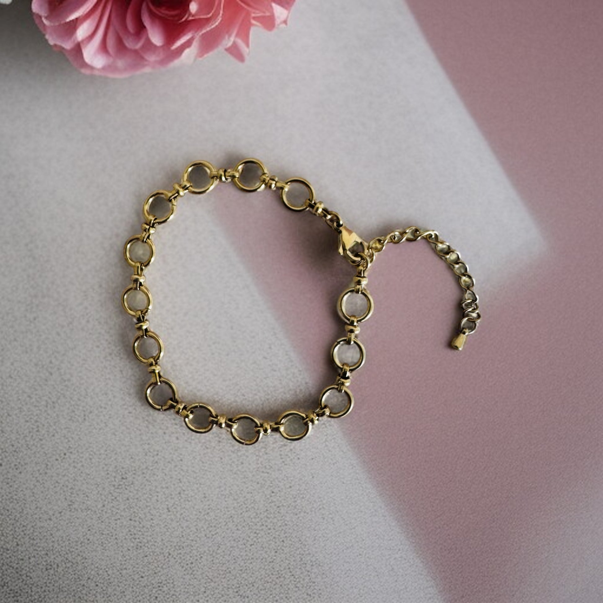 Gold chain anklet  on a light pink surface with a pink flower in the corner.