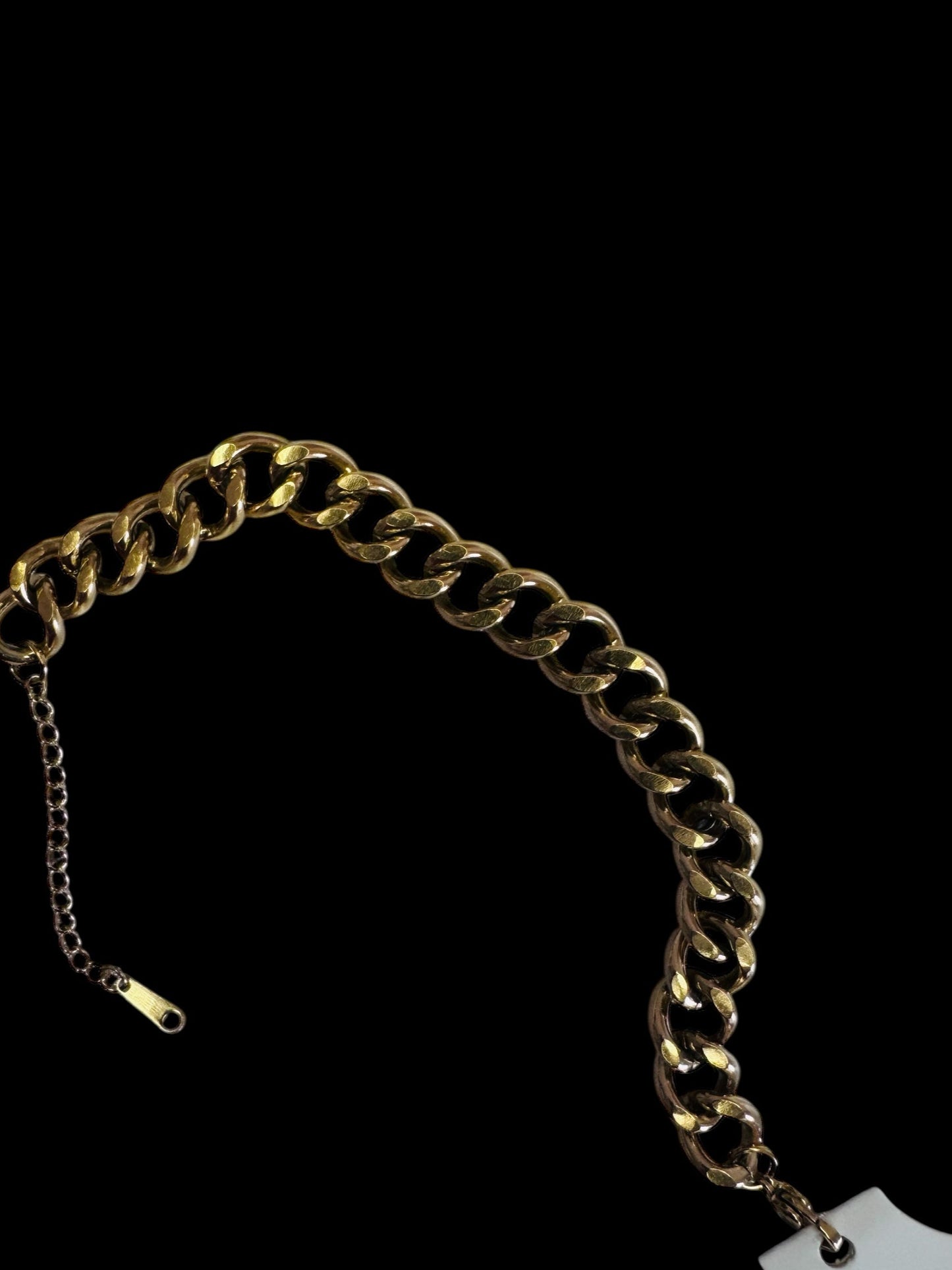 Gold chain anklet with a tag on a black background