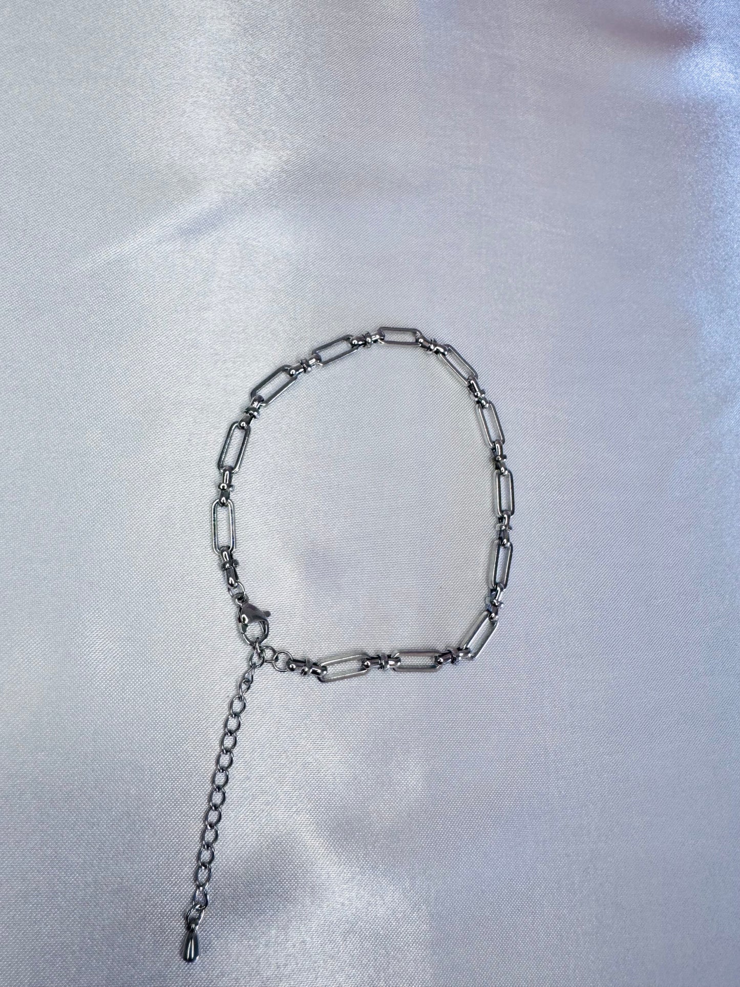 Silver bold link anklet on a white satin background
