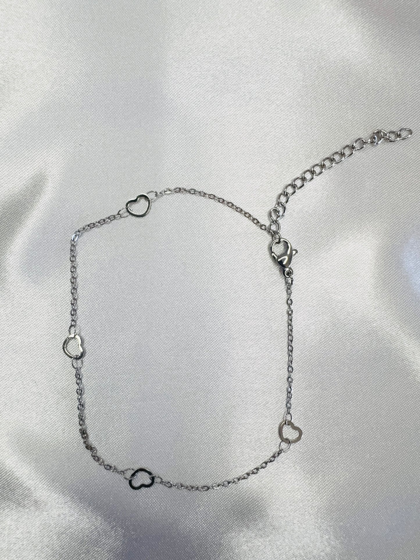 Silver anklet with heart-shaped charms on a light gray background