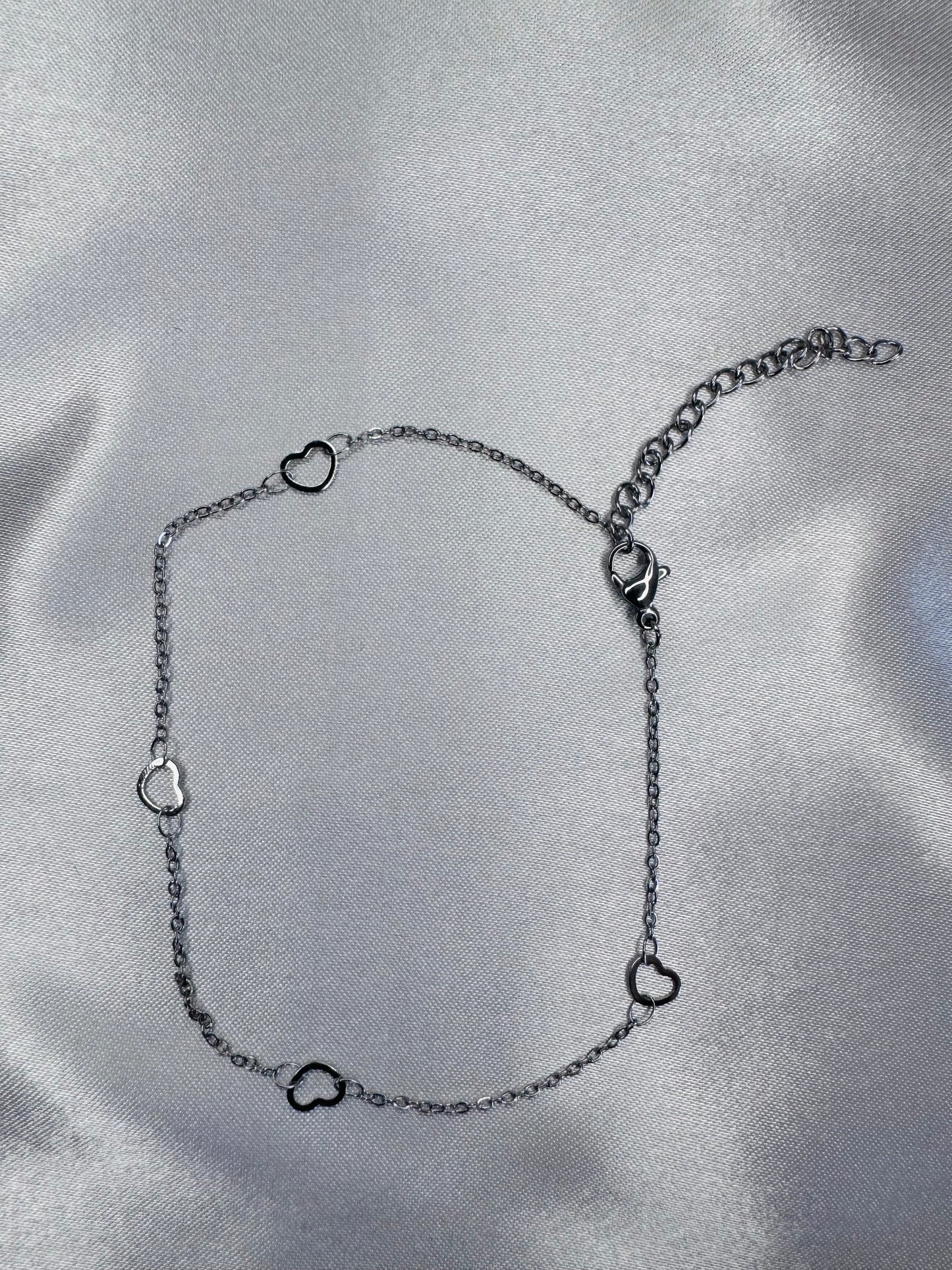 Silver anklet with heart-shaped links on a satin surface