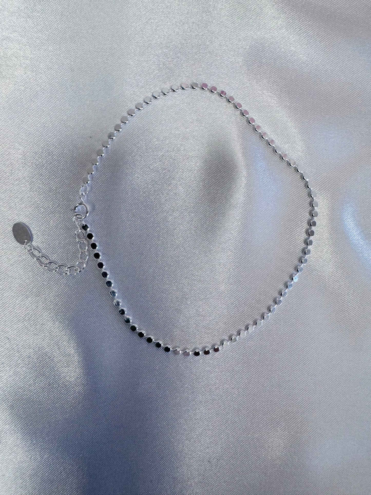 Silver shimmer anklet on a light gray fabric background