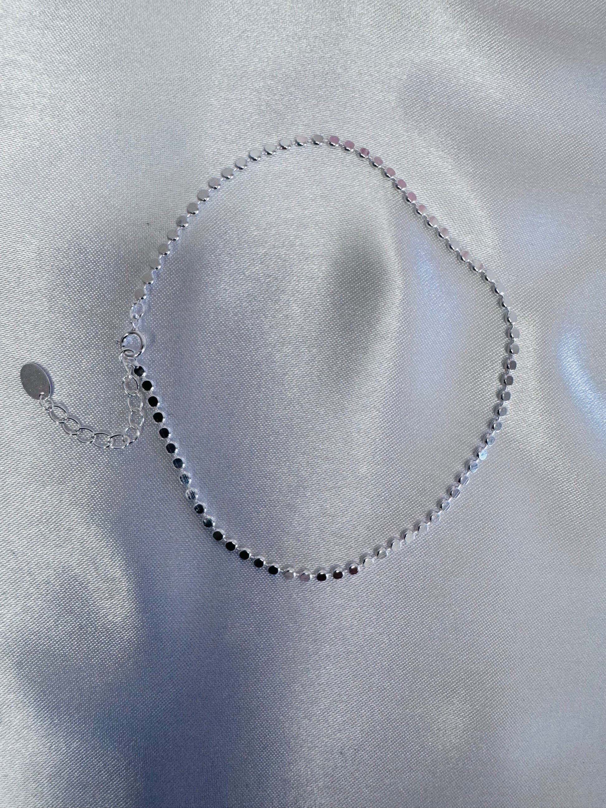 Silver shimmer anklet on a light gray fabric background