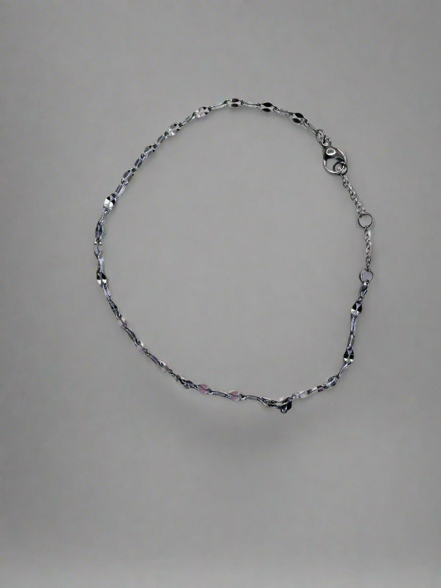 Silver twinkle anklet on a light gray fabric background