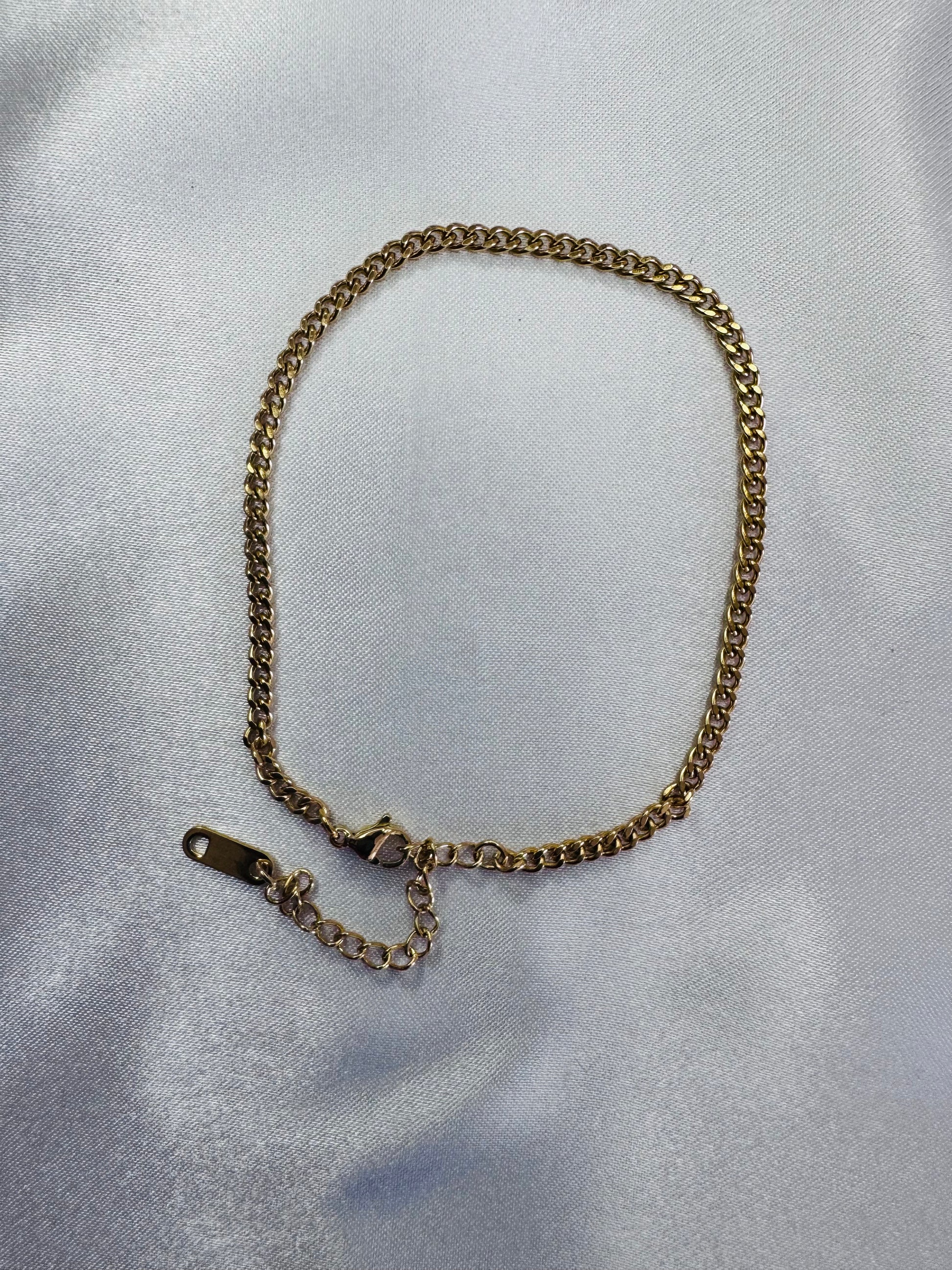 Gold chain anklet on a light gray fabric background