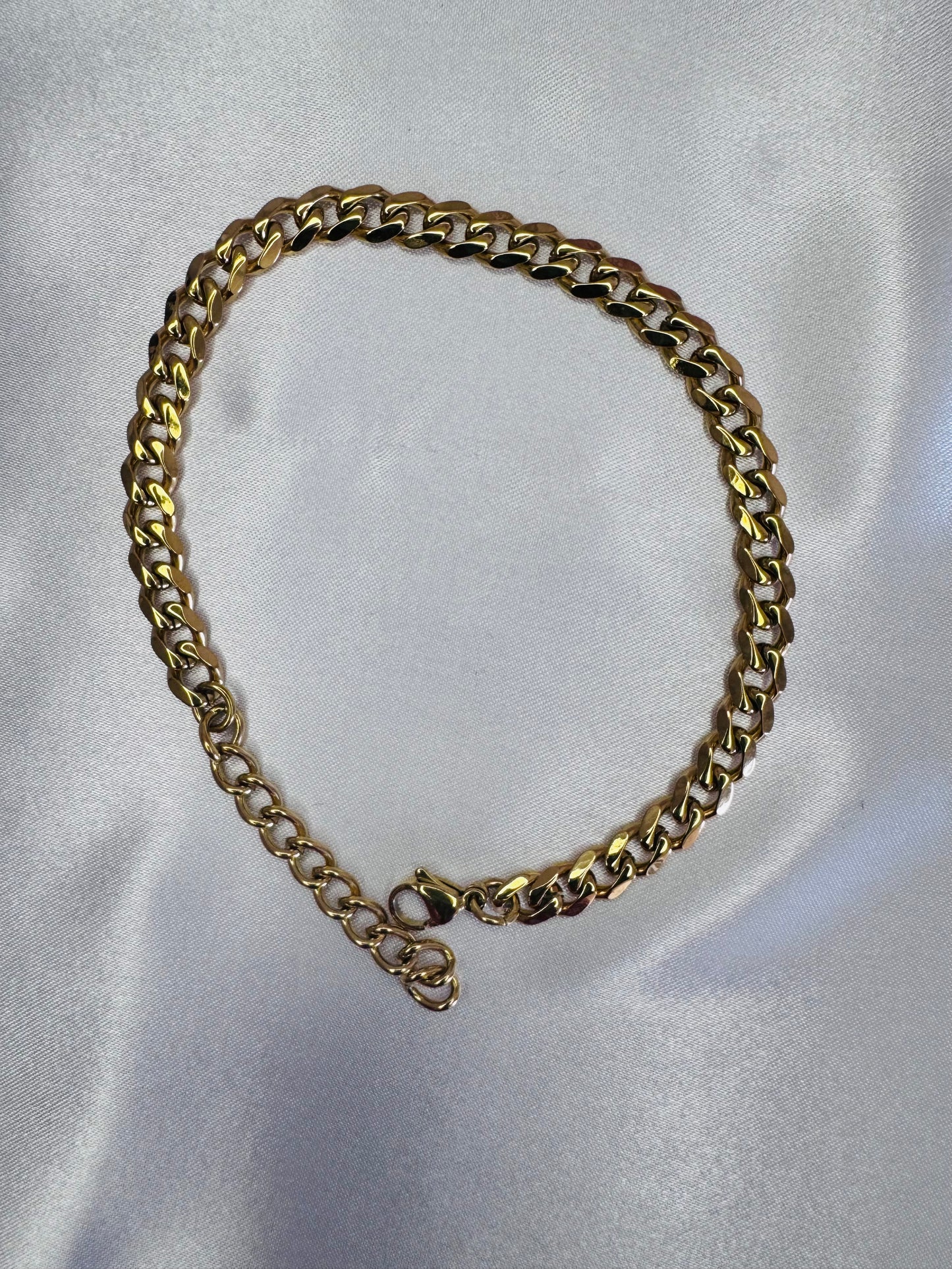 Gold chain anklet on a white satin background