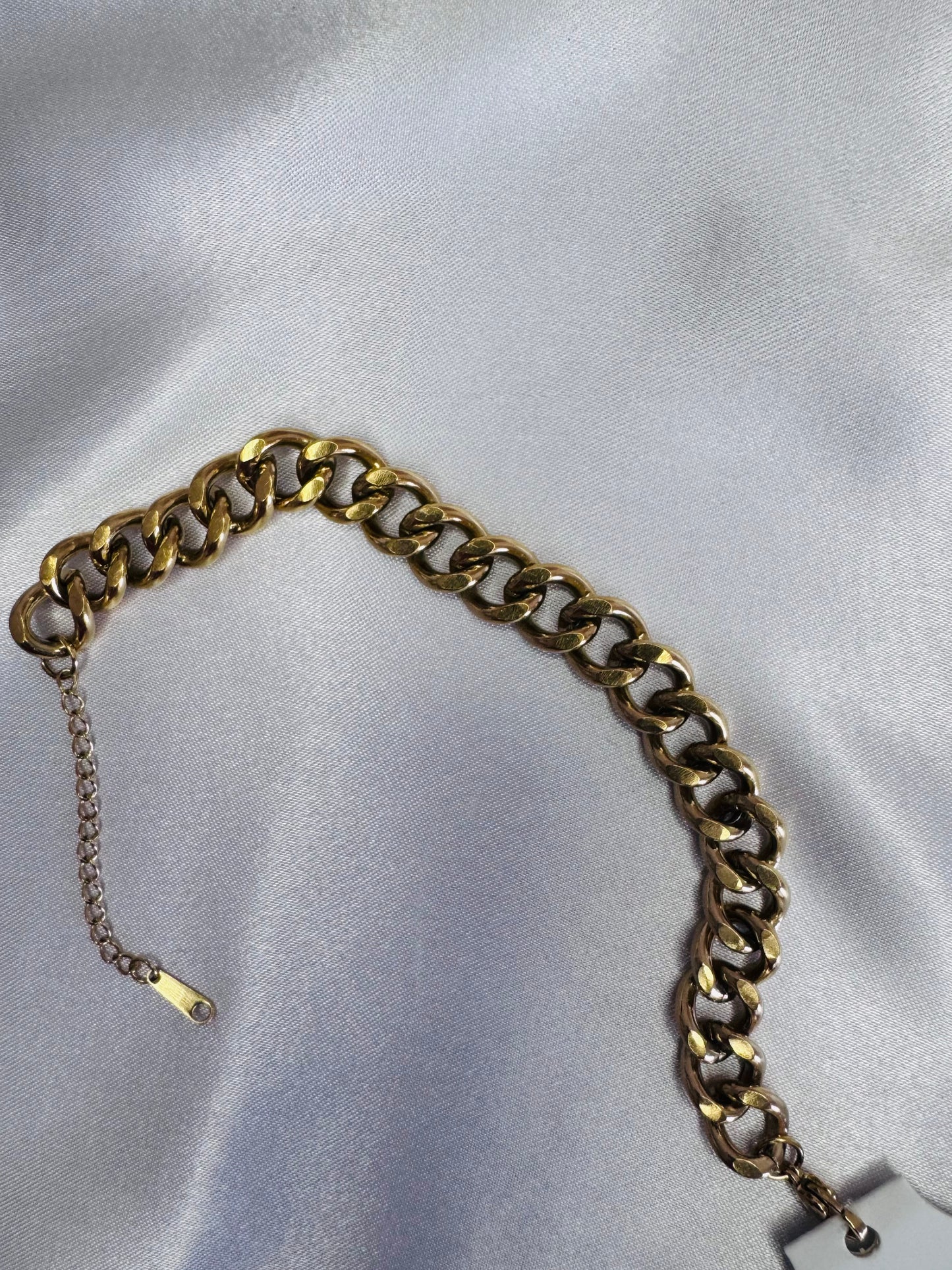 Gold chain anklet on a light gray fabric background