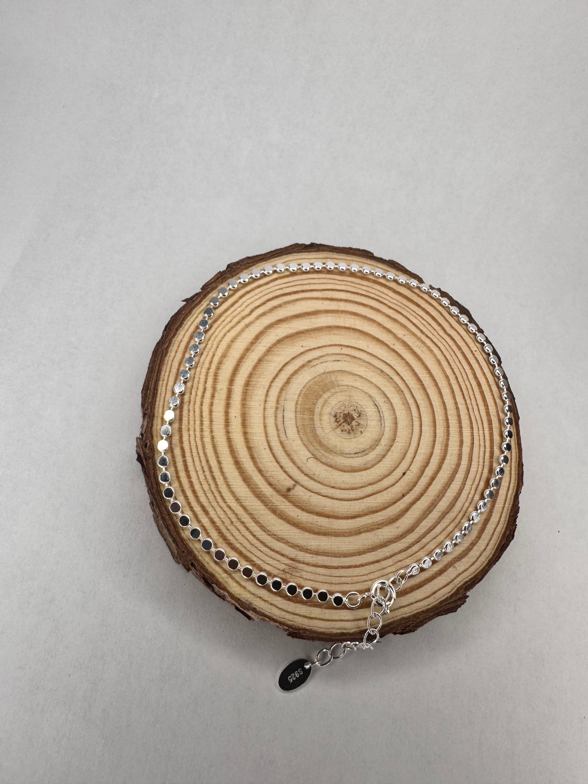 Silver shimmer anklet on a wooden log slice against a gray background