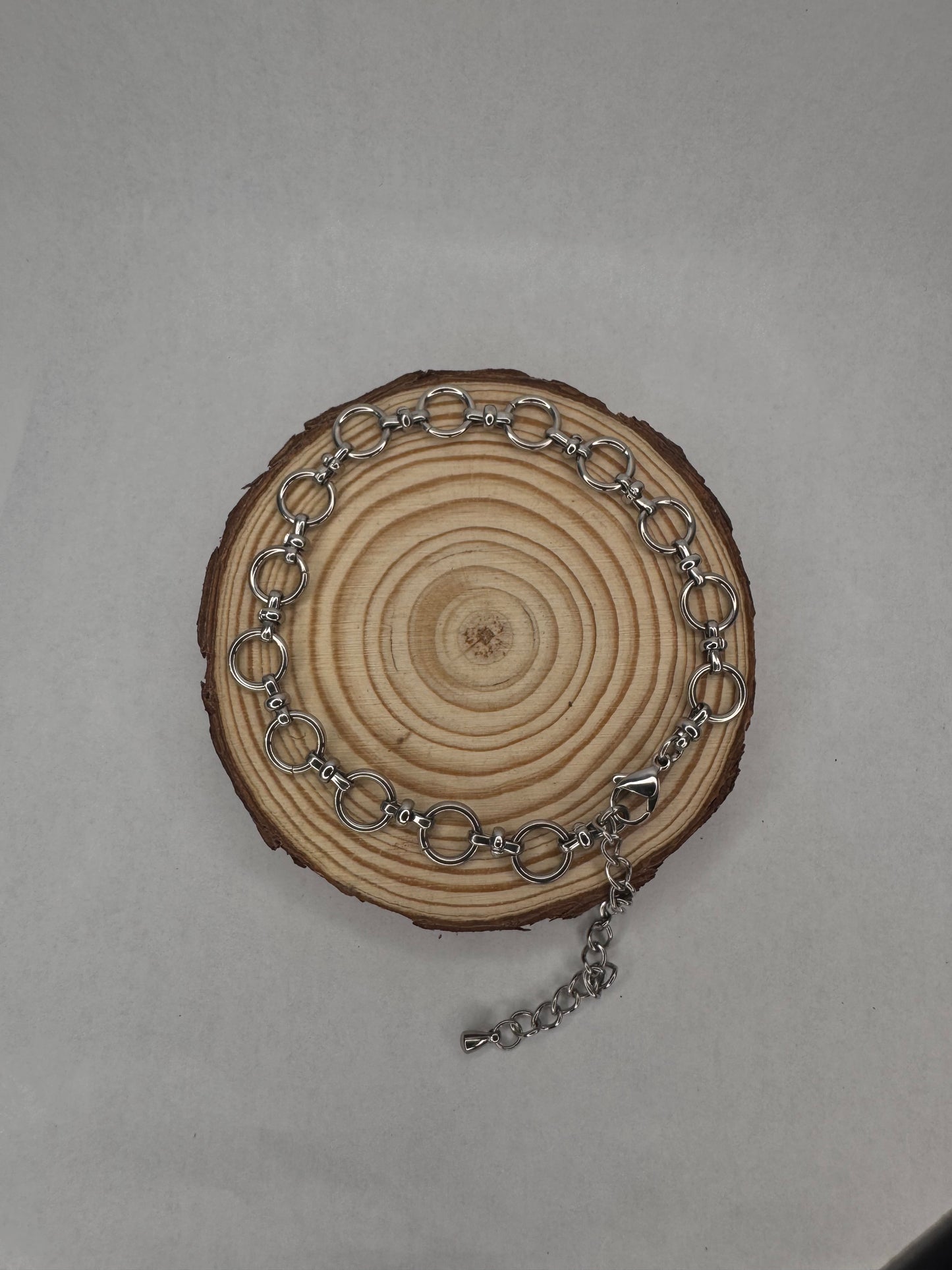 Silver chain anklet on a wooden circular piece with a plain background