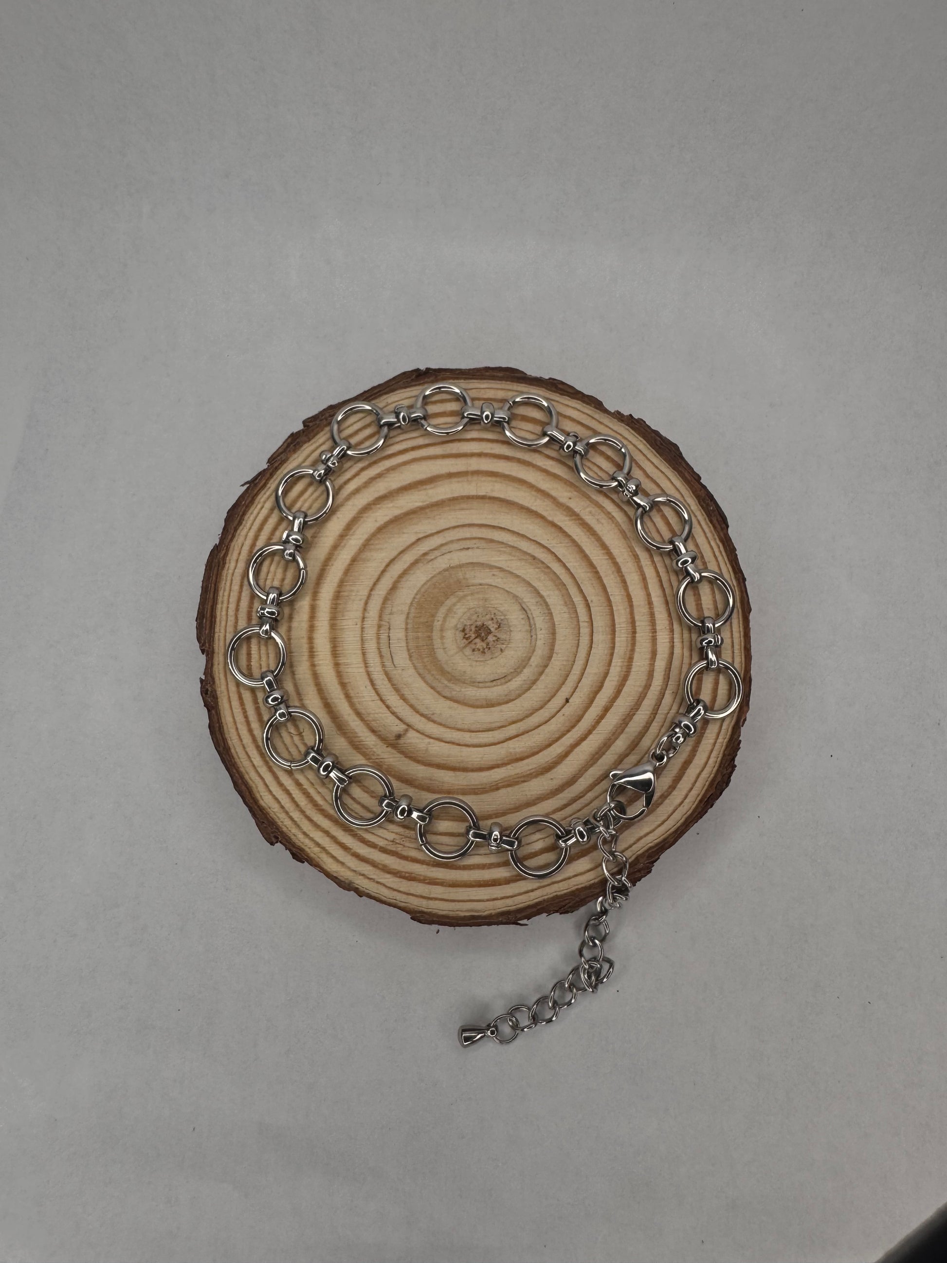 Silver chain anklet on a wooden circular piece with a plain background